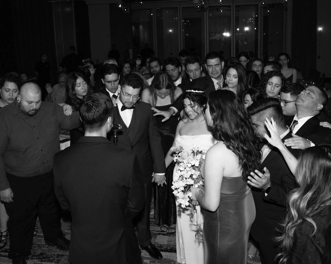 People at a wedding reception praying or blessing during the ceremony with their hands raised and eyes closed.