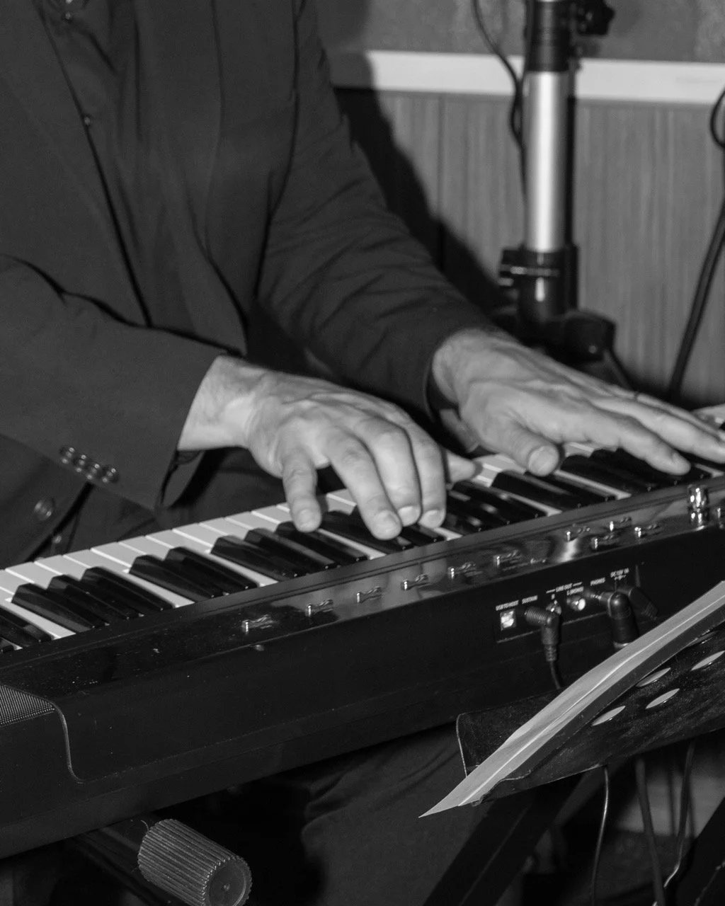 Hands playing a keyboard or digital piano, with sheet music on a stand in front.
