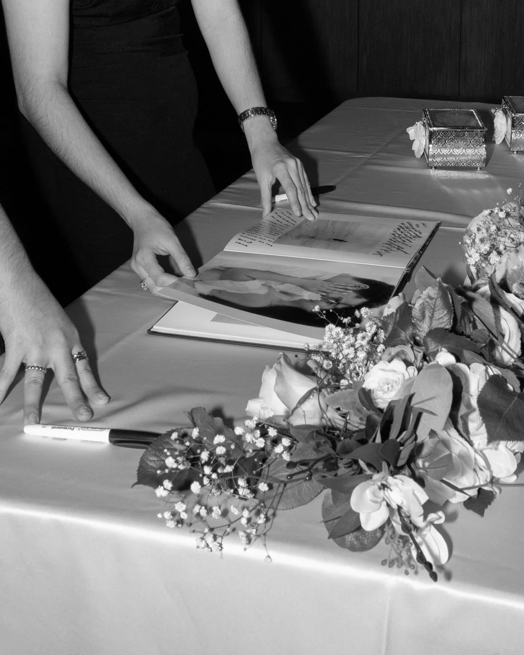 A person flipping through a photo album on a table decorated with flowers and small gift boxes at a celebration or wedding.