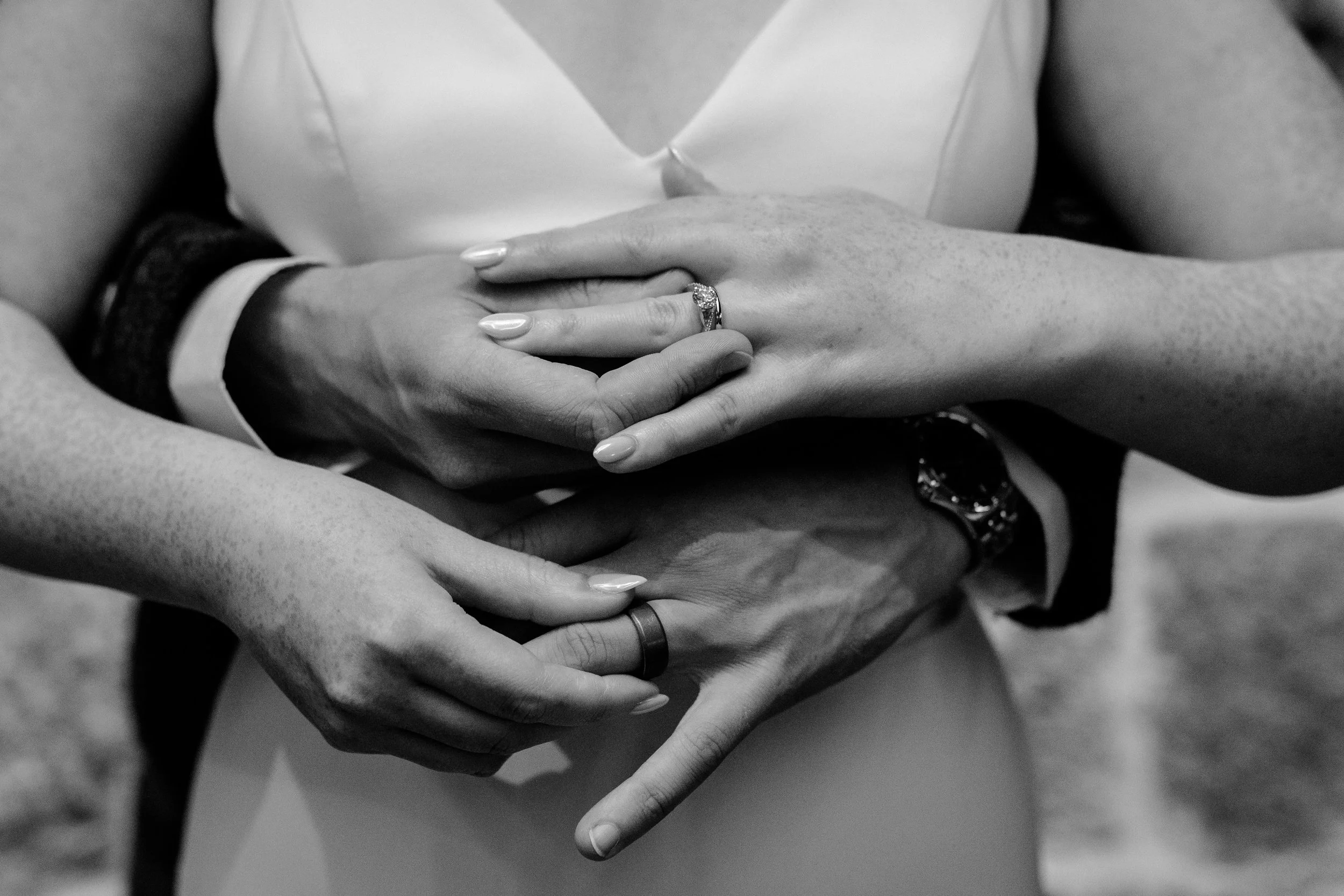 Close-up of four people’s hands with wedding rings, forming a heart shape.