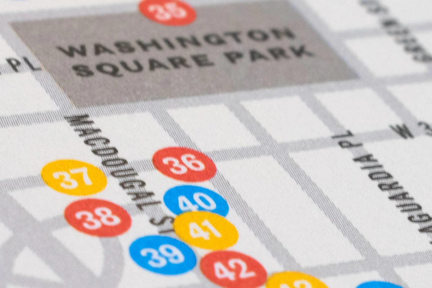 Close-up of a subway map showing the Washington Square Park station and nearby stops with numbered circles in red, yellow, and blue.