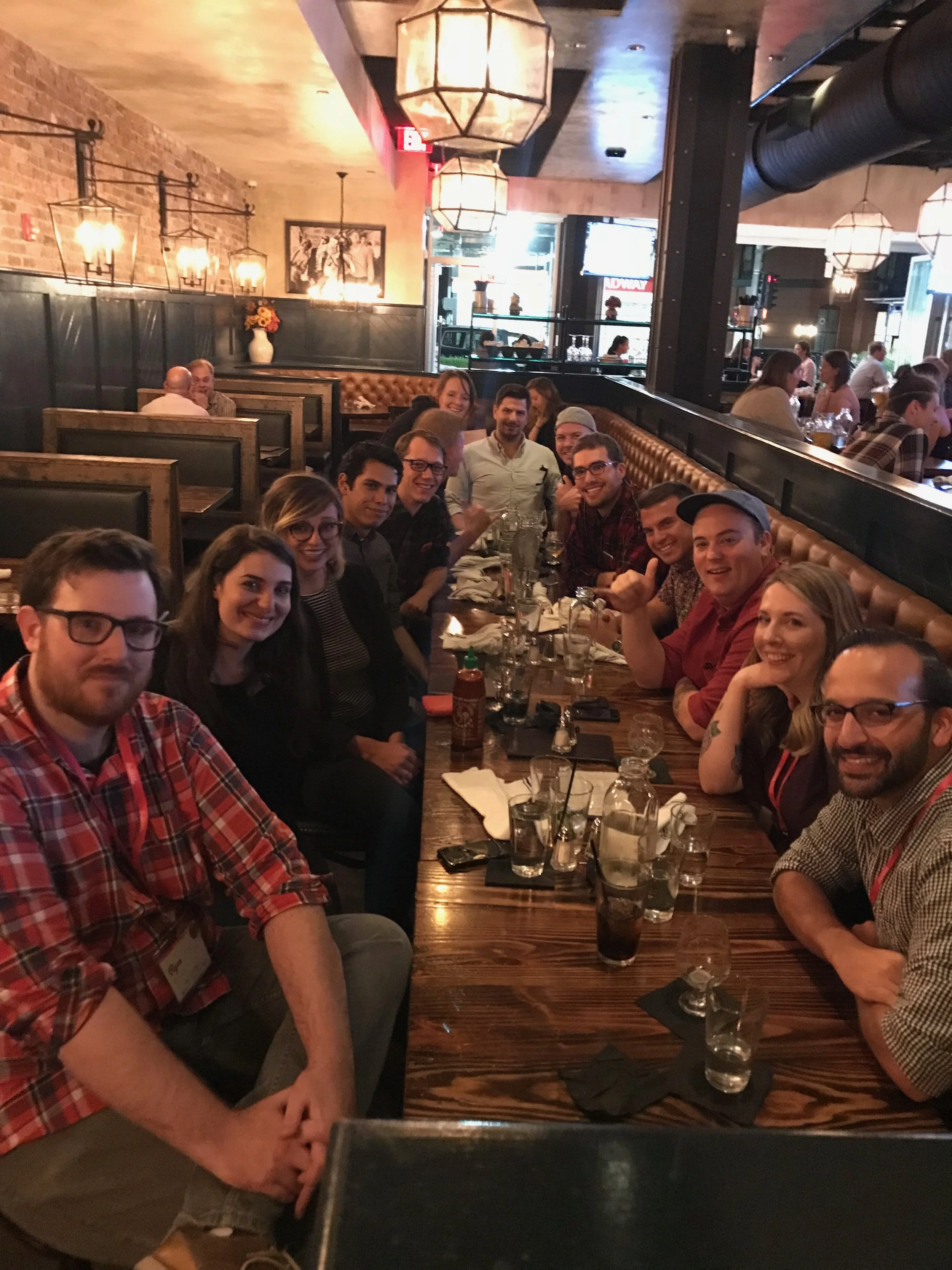 A group of people sitting at a long wooden table in a restaurant, smiling for the photo.