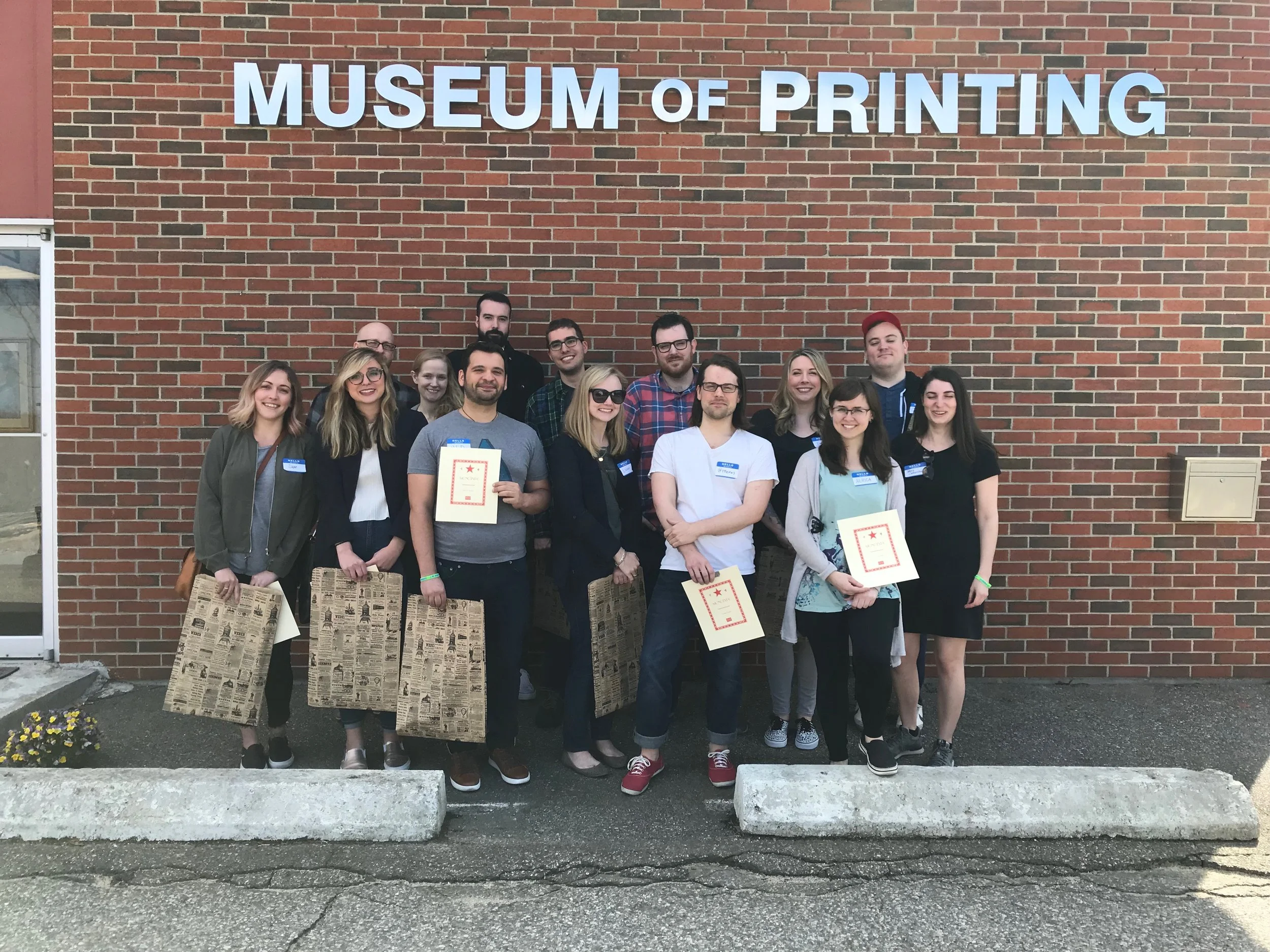 Group of people standing outside the Museum of Printing, some holding certificates, posing for a photo in front of a brick wall with the museum's sign.