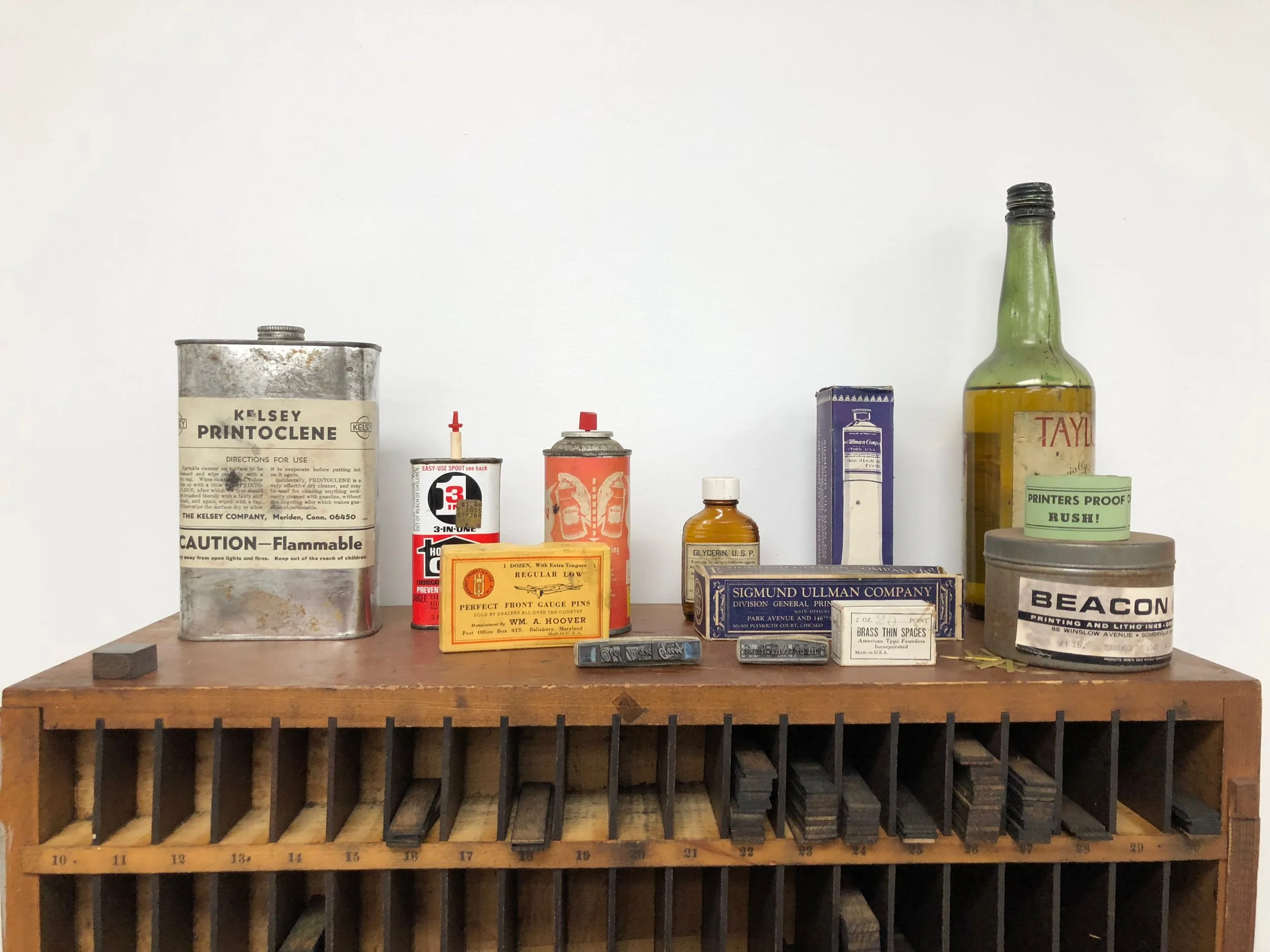 Collection of vintage ink and printing supplies on wooden shelf, including ink cans, bottles, and boxes.