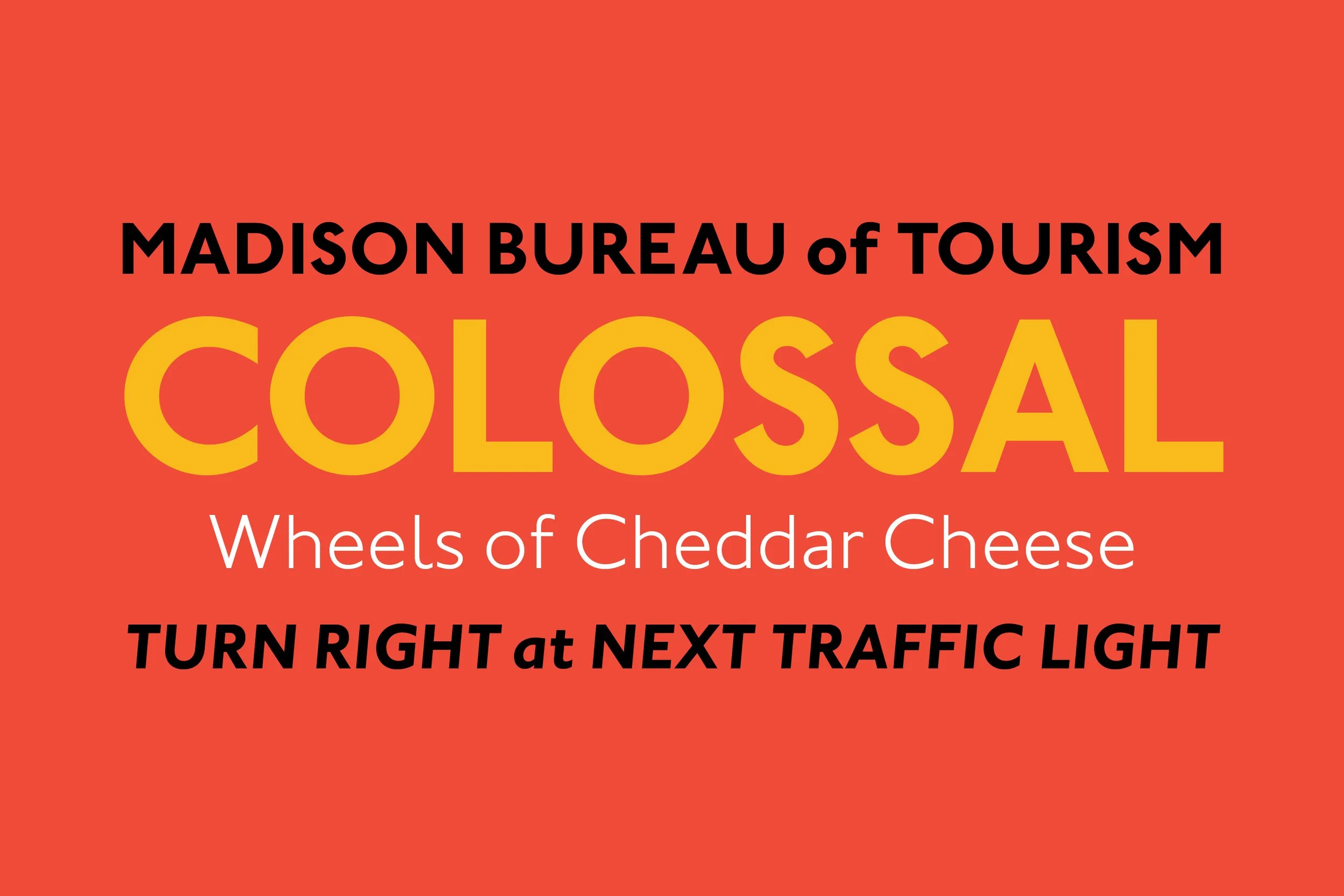 Sign for Madison Bureau of Tourism promoting a colossus pizza with wheels of cheddar cheese, instructing to turn right at the next traffic light.