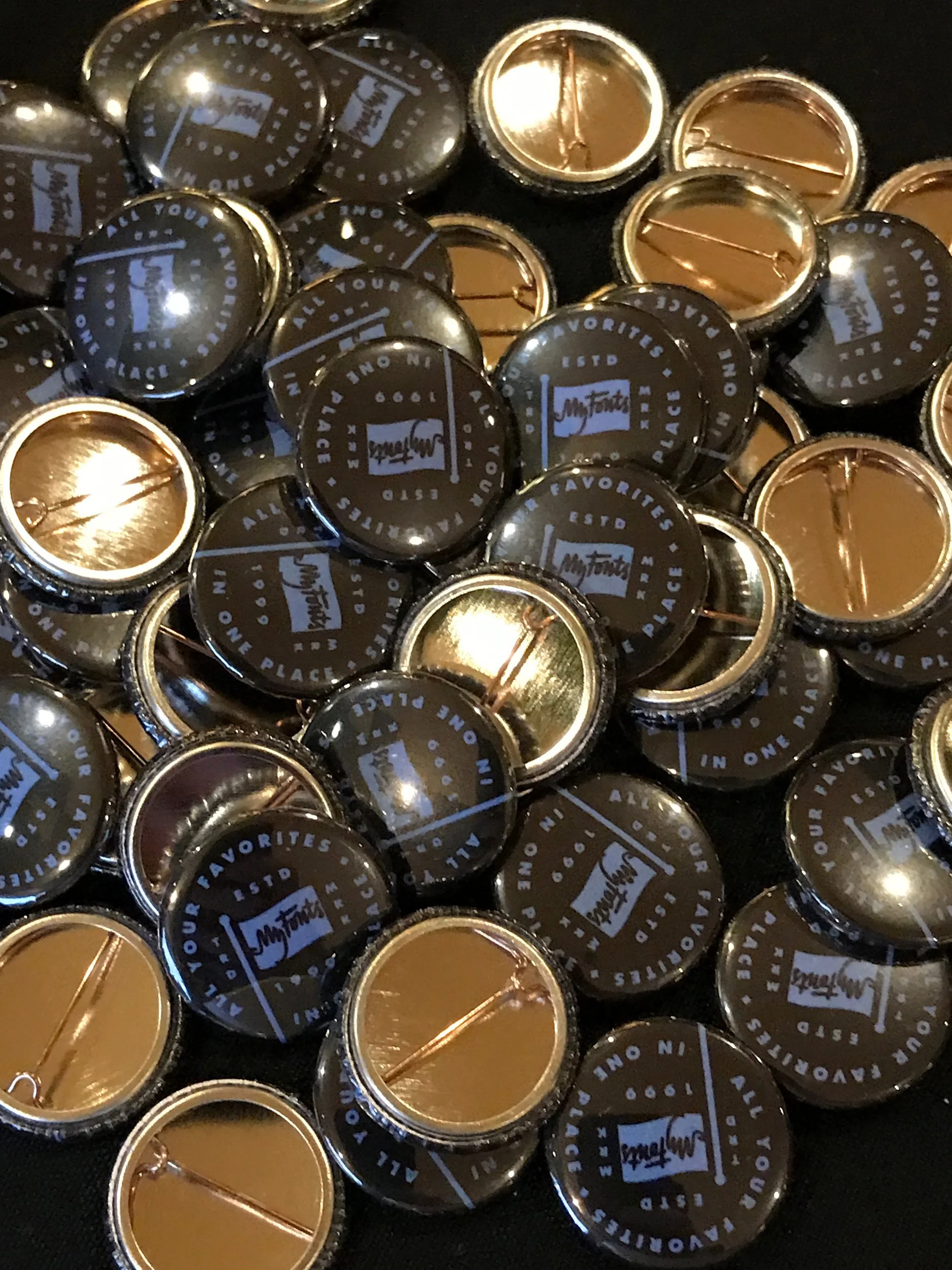 A collection of black and gold pins with the text 'My Totts' and 'Your favorites, one place, ESTD 1999' on the front.