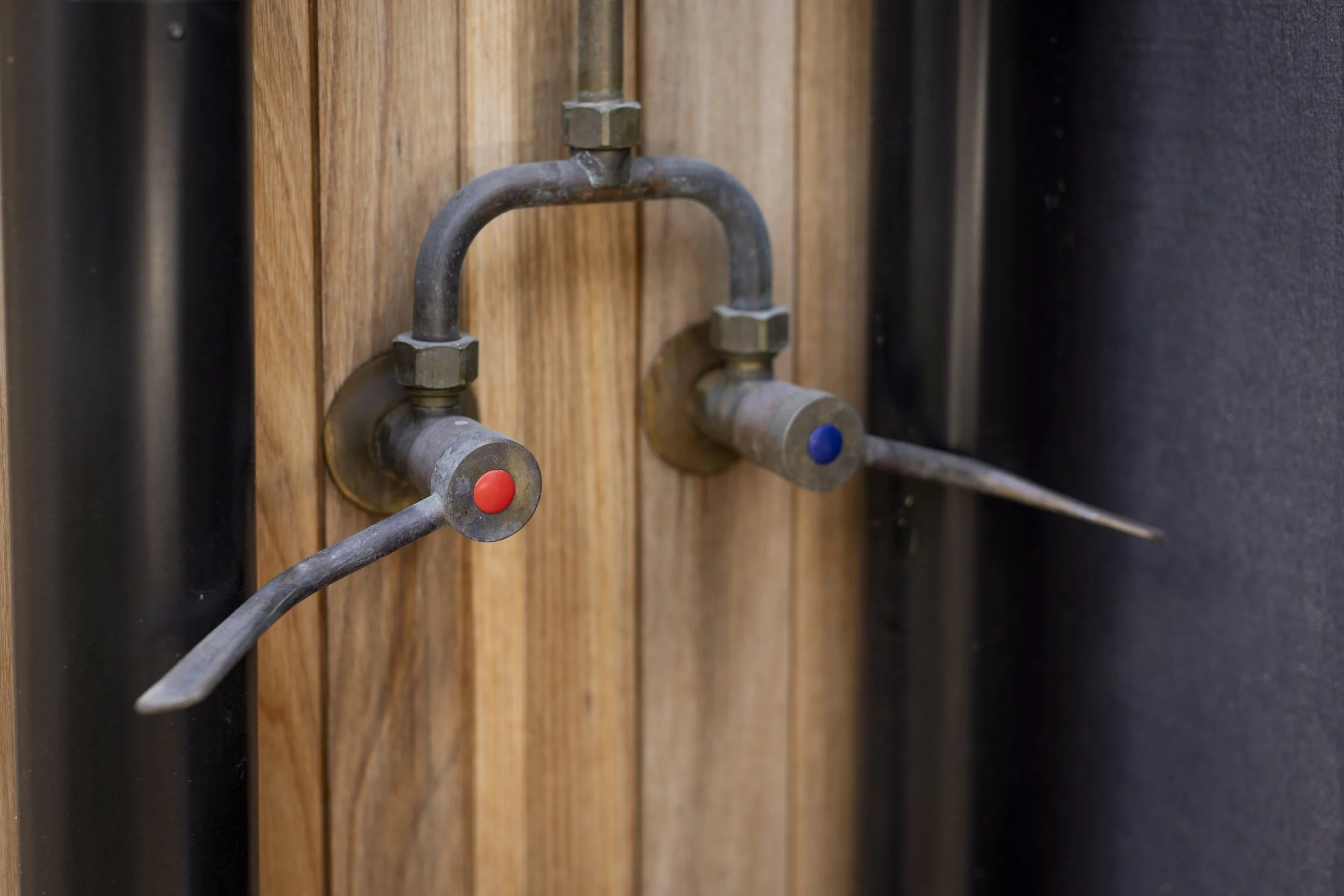 Close-up of metallic pipes with red and blue nozzles mounted on a wooden wall.