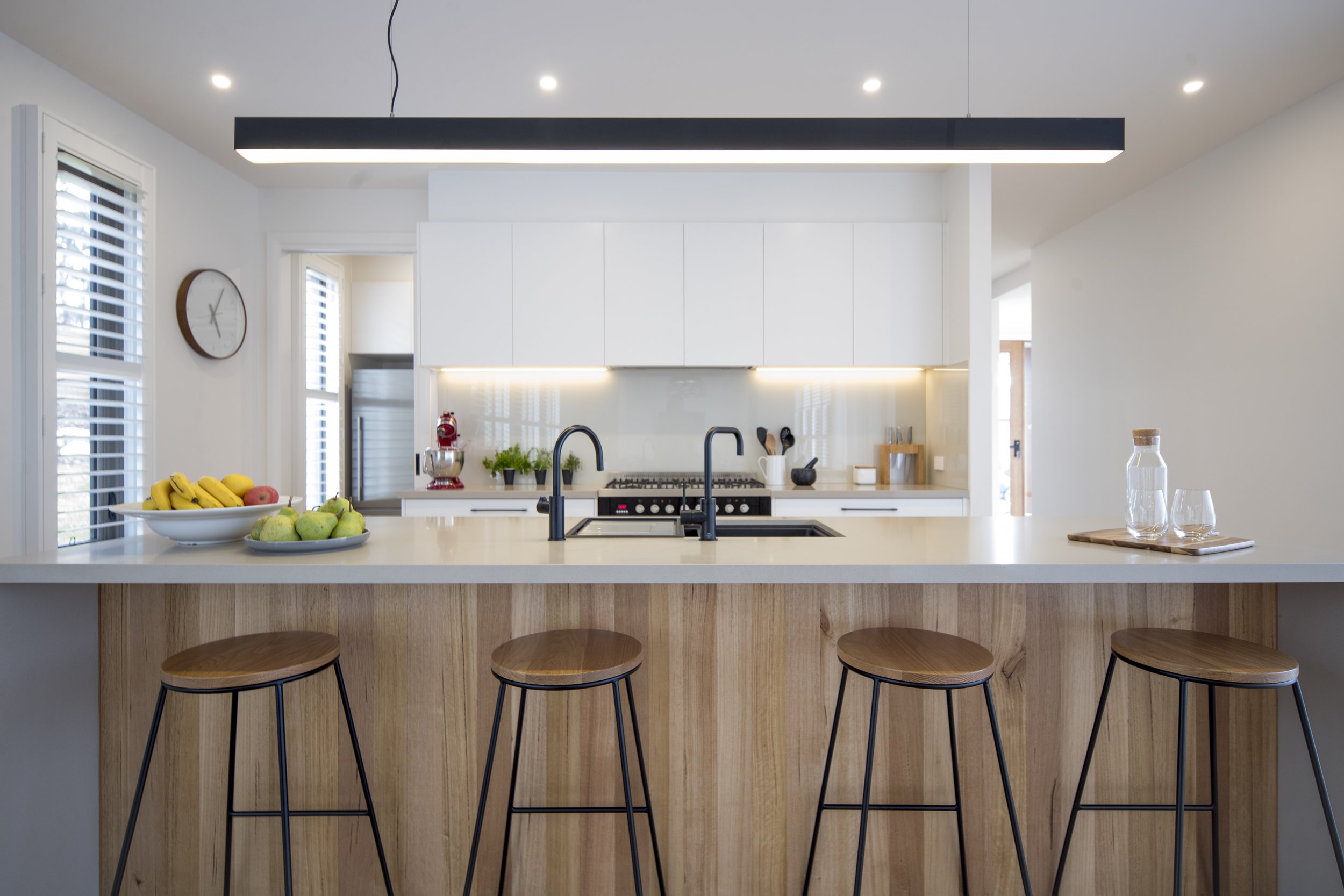 Modern kitchen with white cabinets, black faucet, fruit bowl, bar stools, and pendant light fixture
