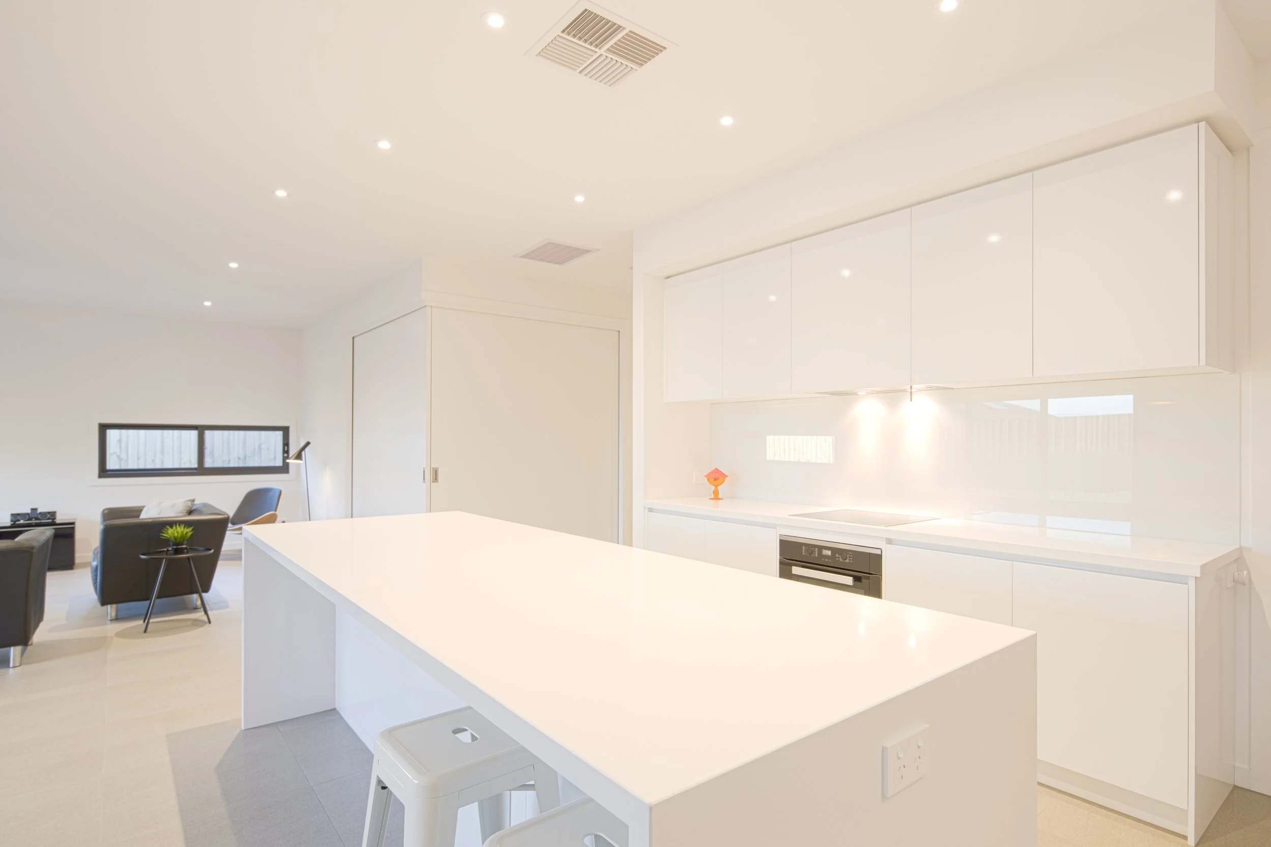 Modern kitchen with white cabinets, island, and built-in appliances, open to living area with seating and large window.