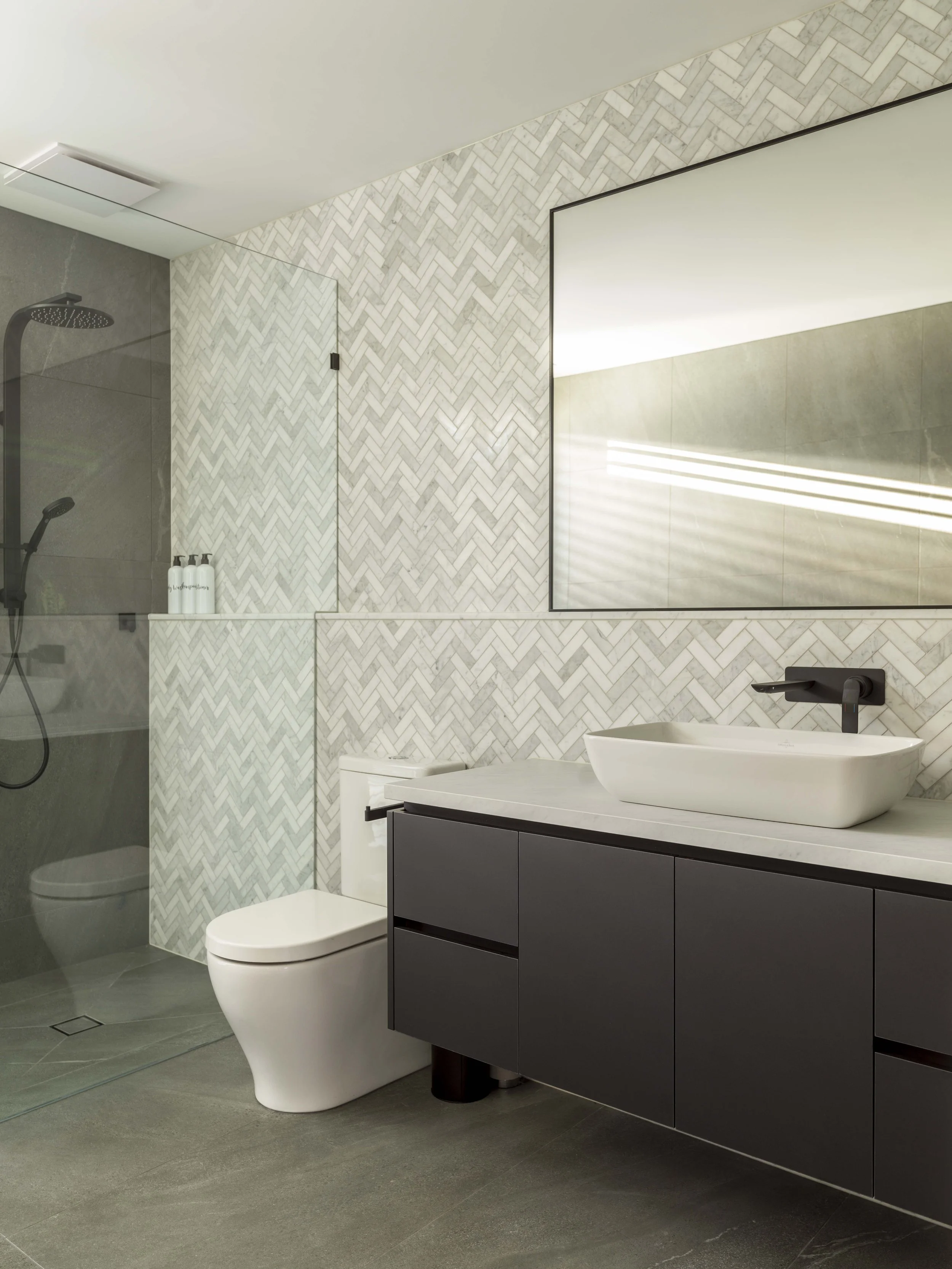 Modern bathroom with walk-in shower, toilet, black vanity with sink, large mirror, and patterned tile wall.