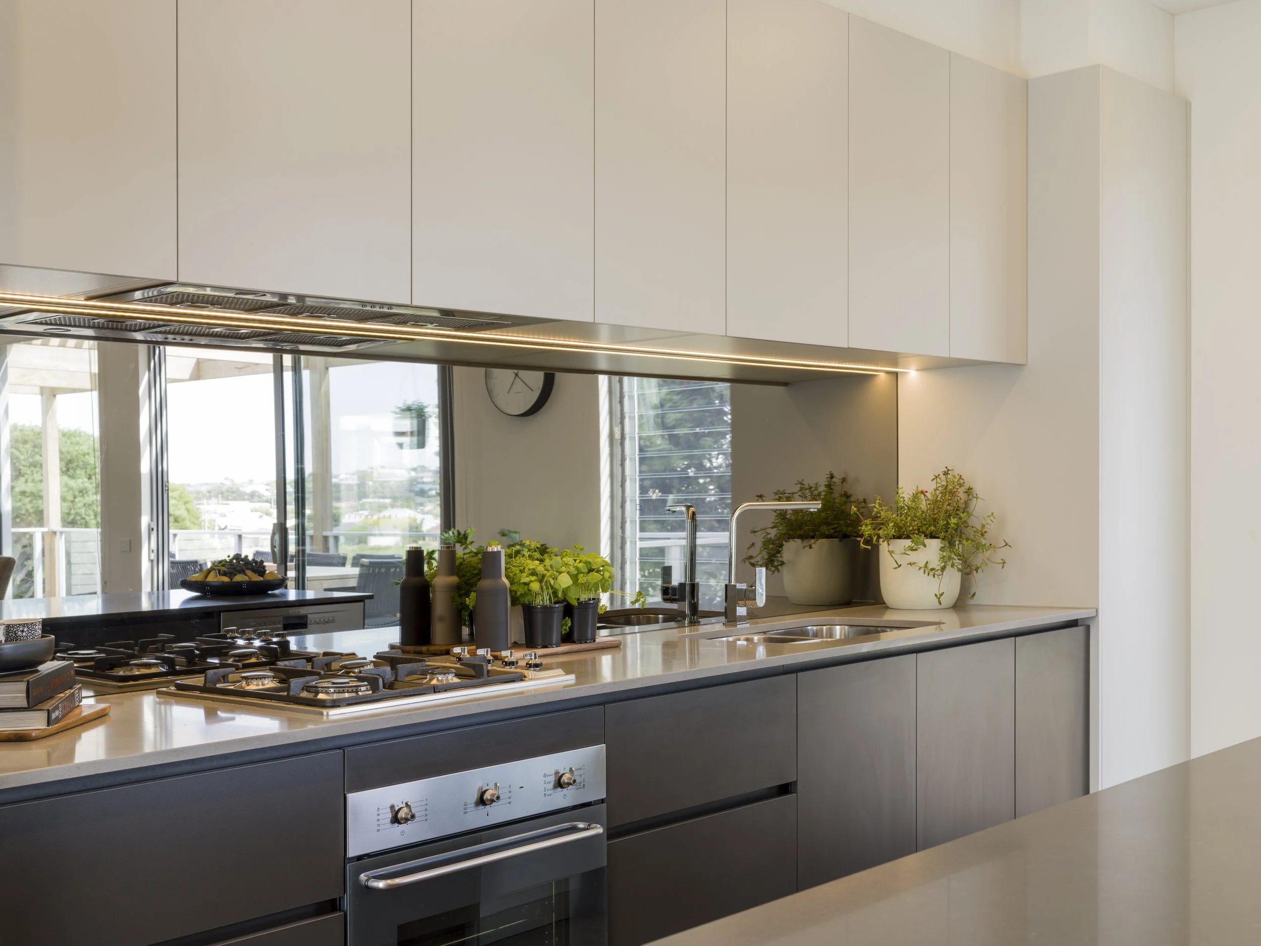 Modern kitchen with a gas stove, potted plants on the countertop, and large windows providing natural light.