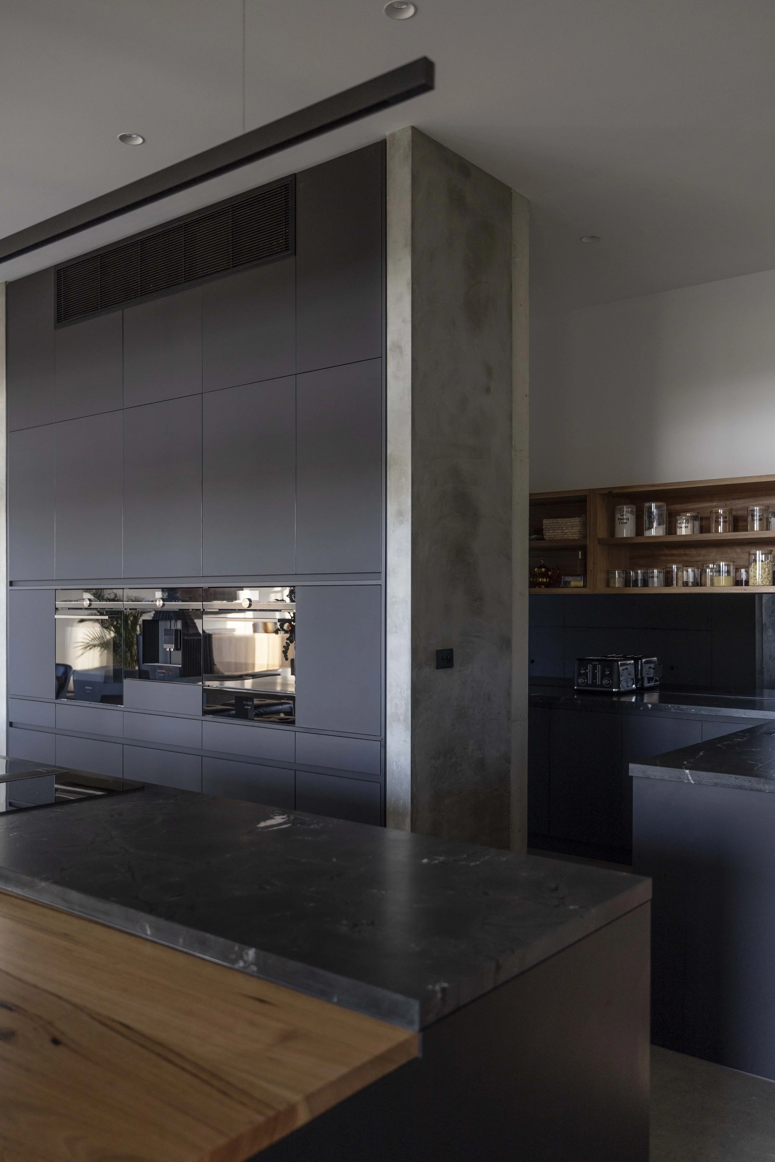 Modern kitchen interior with black countertop, wooden drawer, gray tiled cabinets, and open wooden shelves with glass jars.
