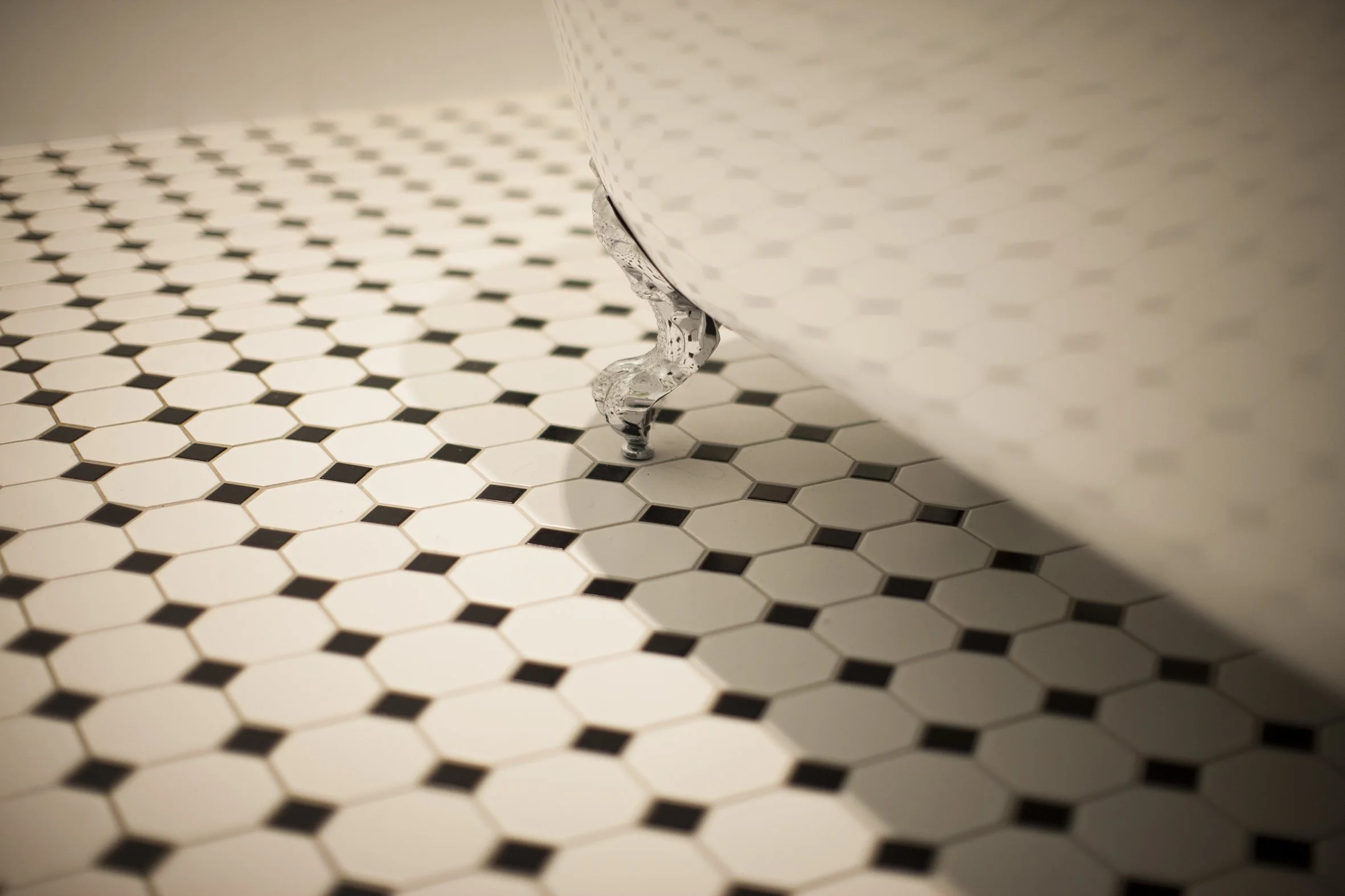 Close-up of a clawfoot bathtub with water dripping from its ornate leg, set on a white and black hexagonal tiled floor.