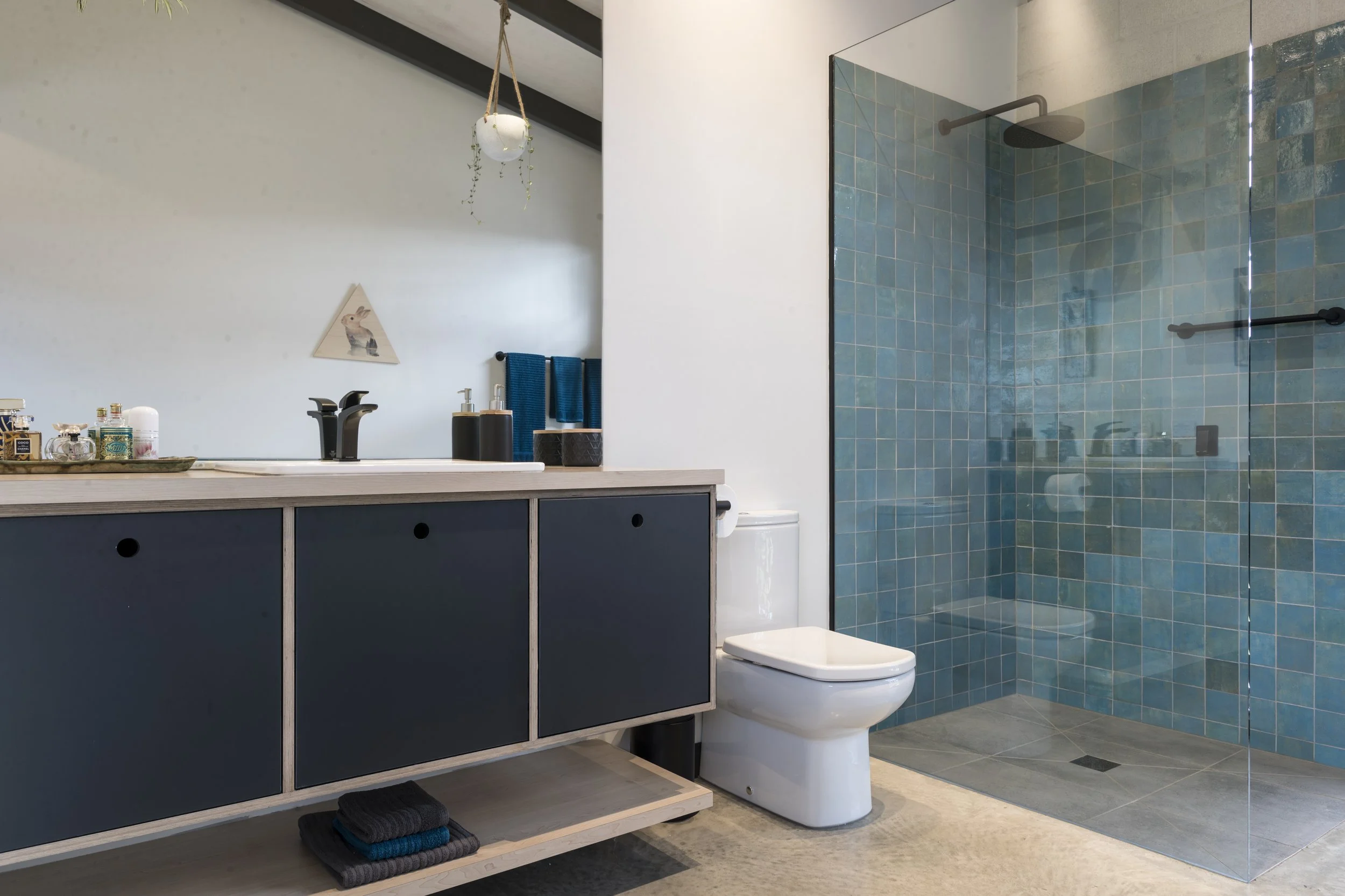Modern bathroom with a blue vanity, a white toilet, and a walk-in shower with blue tiles and a glass door.