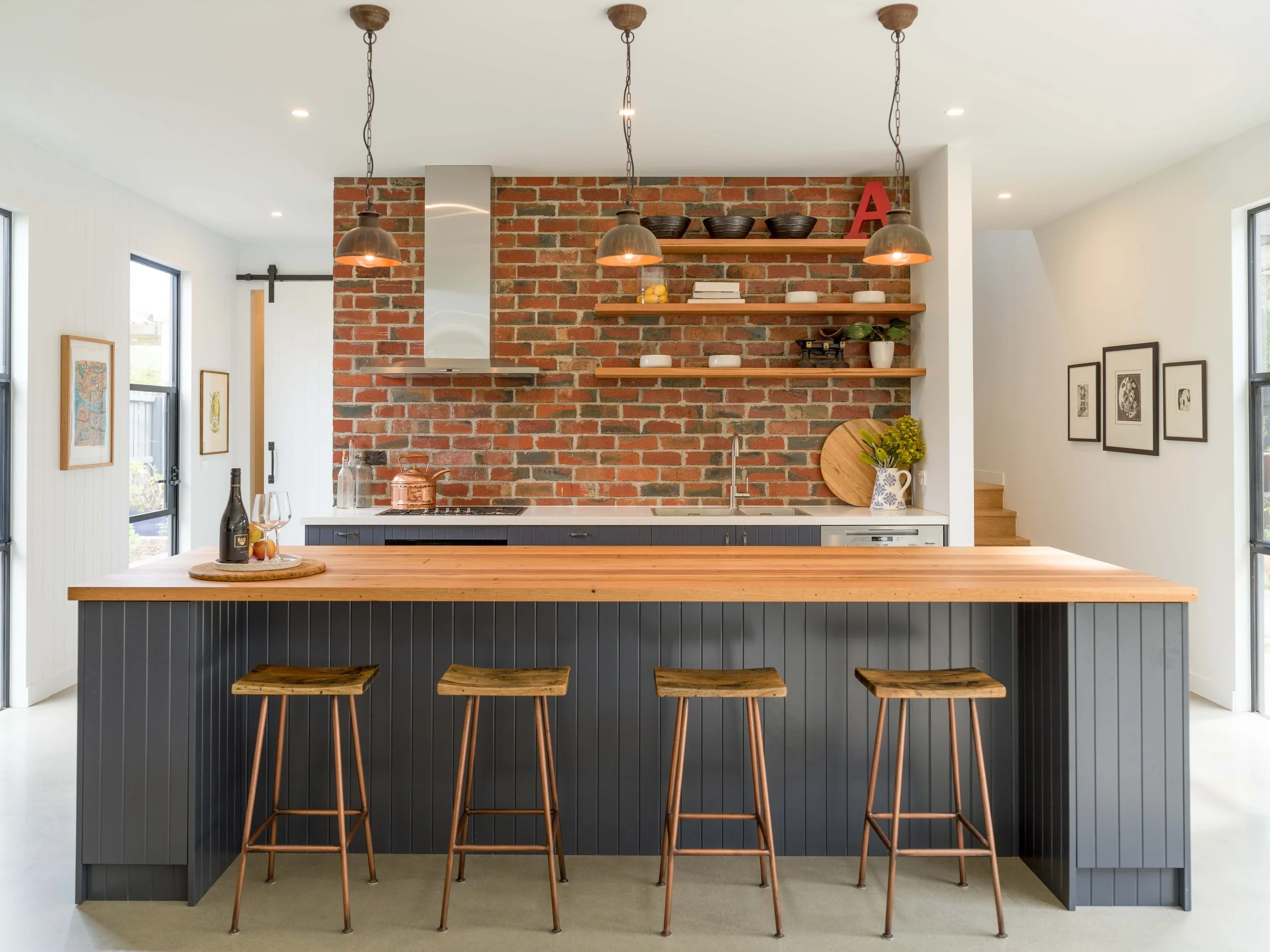Modern kitchen with a brick accent wall, hanging pendant lights, and a wooden kitchen island with four bar stools.
