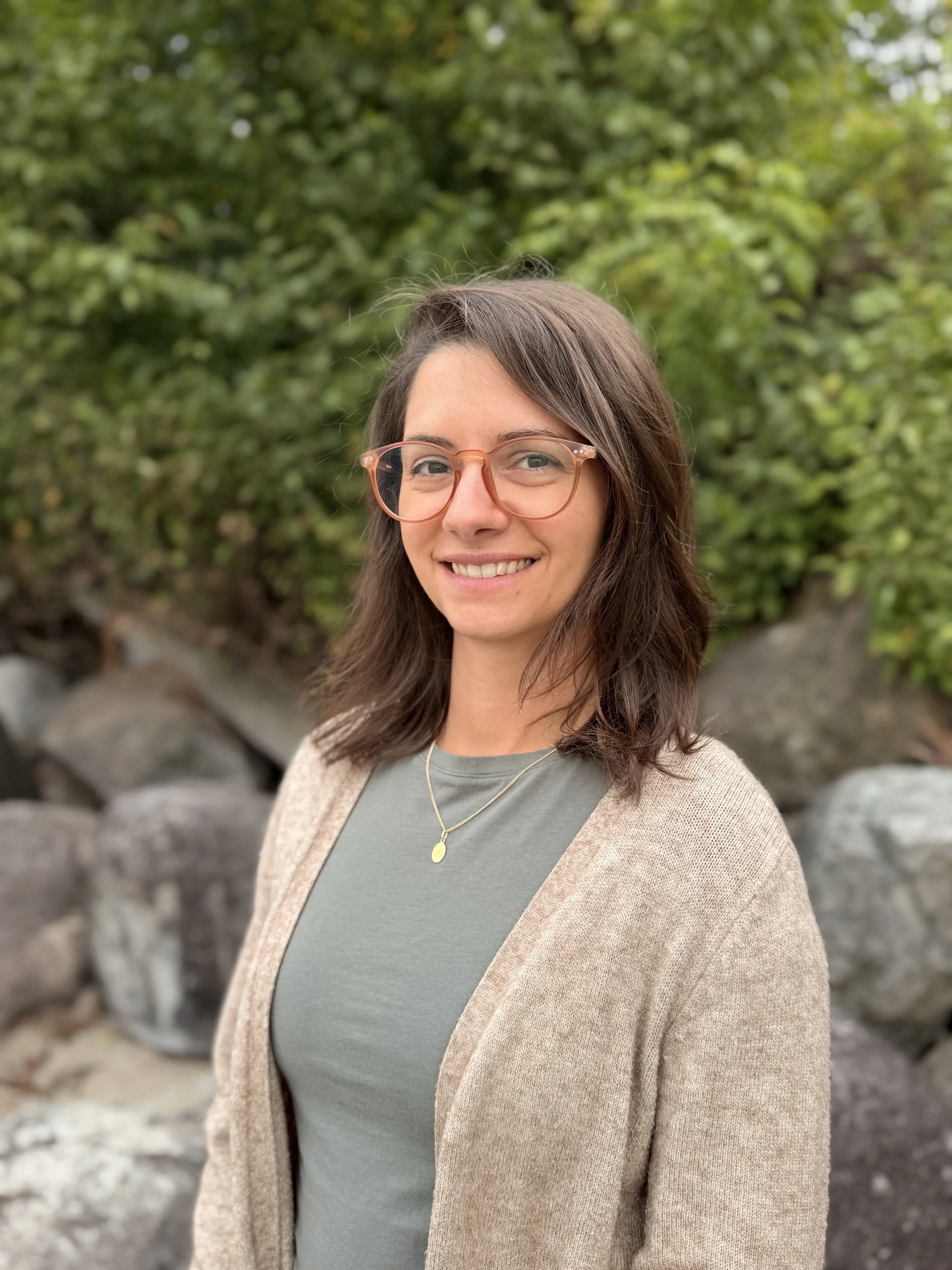 Photo of Nicole Persall, a therapist in Vancouver standing on Kitsilano beach wearing a brown cardigan, glasses, and a warm smile.