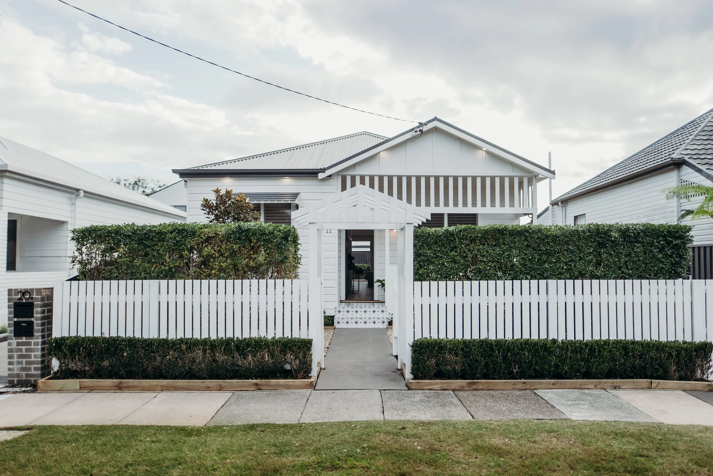 Front exterior of a white house with a white picket fence, gate, and well-maintained greenery.