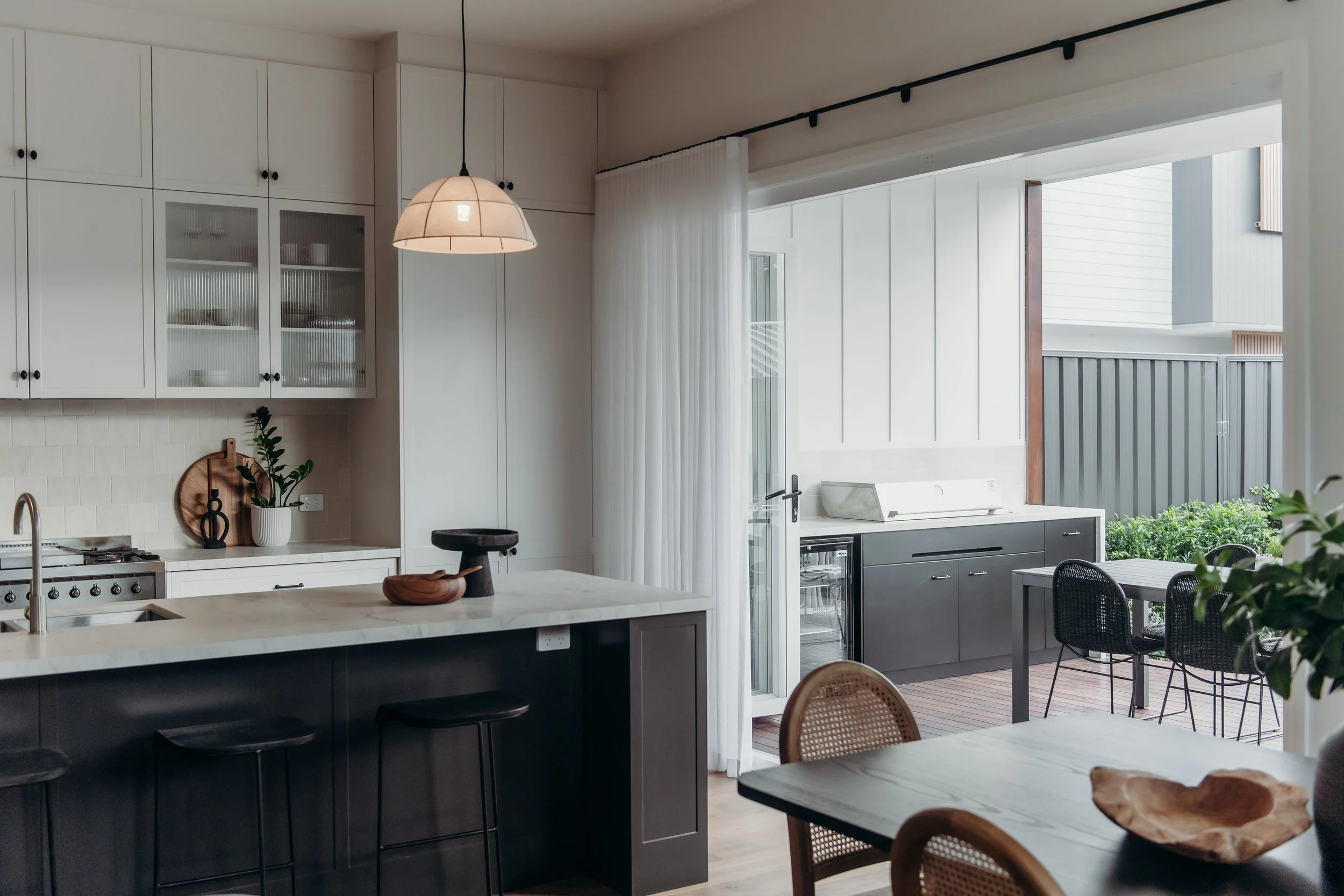 Modern kitchen with white cabinets, black lower cabinets, a marble countertop, and a view of an outdoor patio with black cabinets and a dining table.