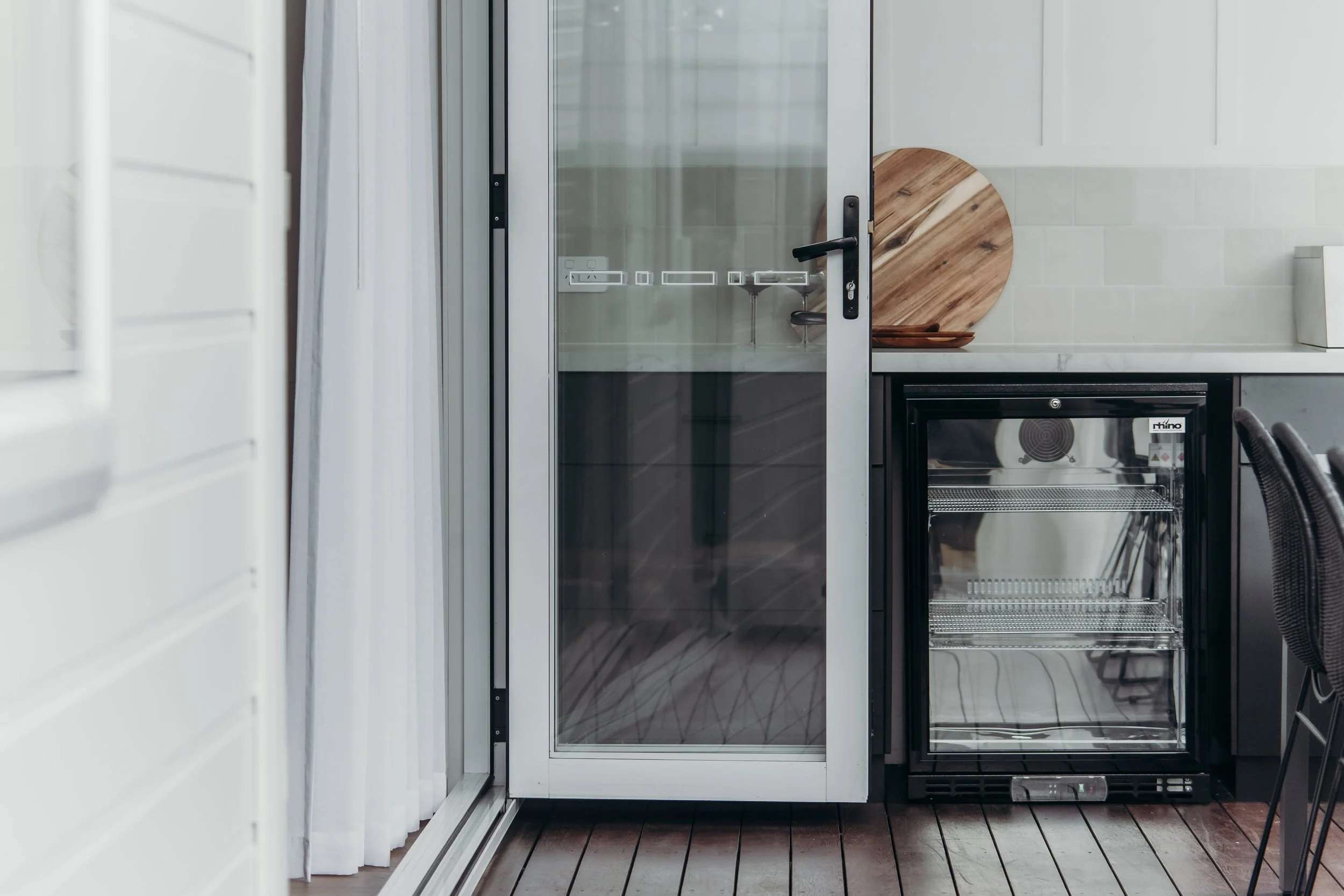 Indoor kitchen area with a glass door, wooden cutting board, and small refrigerator.