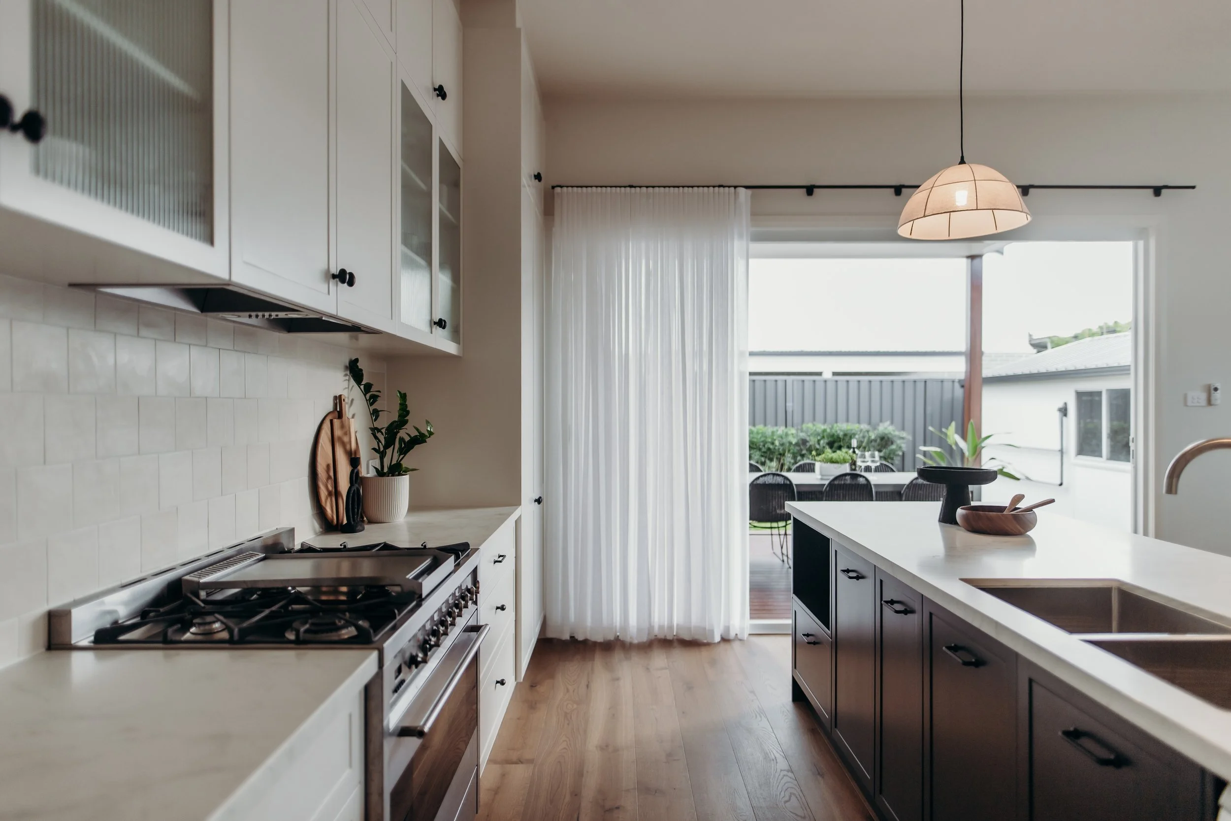 Bright modern kitchen with white cabinets, black countertops, and a view of an outdoor patio with a dining table and greenery.