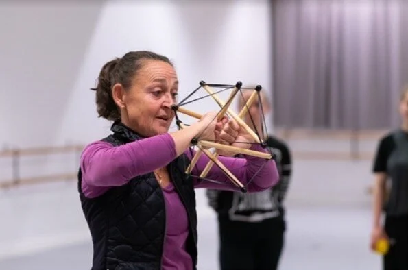 Cecilia Douglas håller ett trä- och snöre-objekt framför sig i ett dans- eller teaterrepetitionsrum.