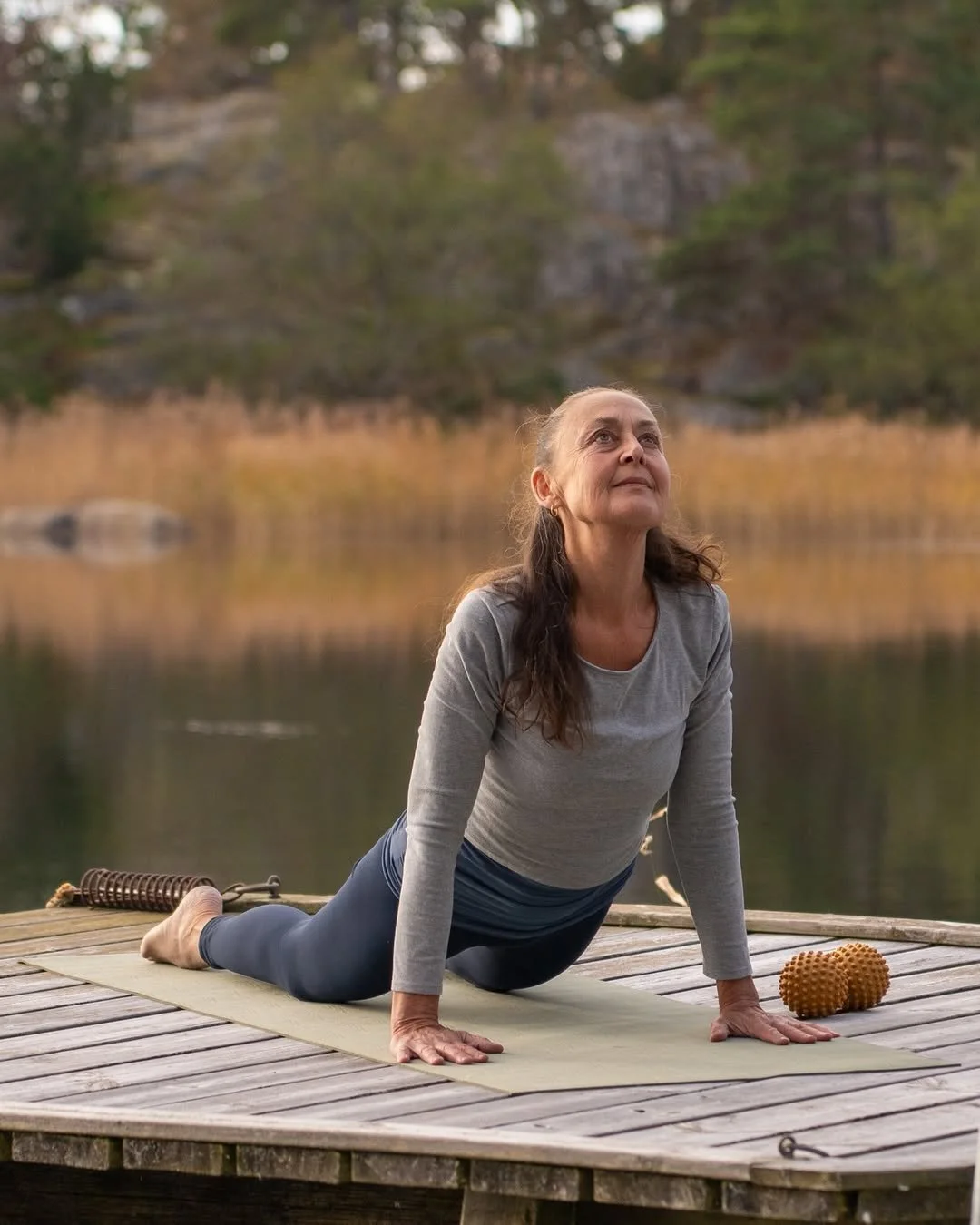 Cecilia Douglas utomhus som utövar yoga på en trädäck, omgiven av natur med vatten och träd i bakgrunden