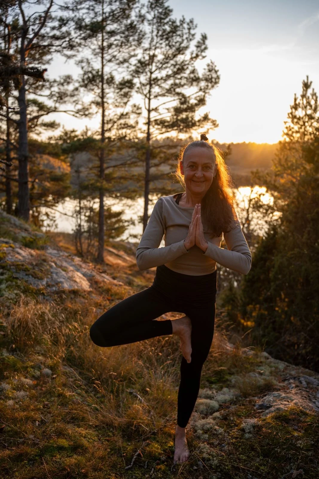 Cecilia Douglas utövar yoga i naturen vid solnedgången, står på ett ben i en trädgårdsposition.