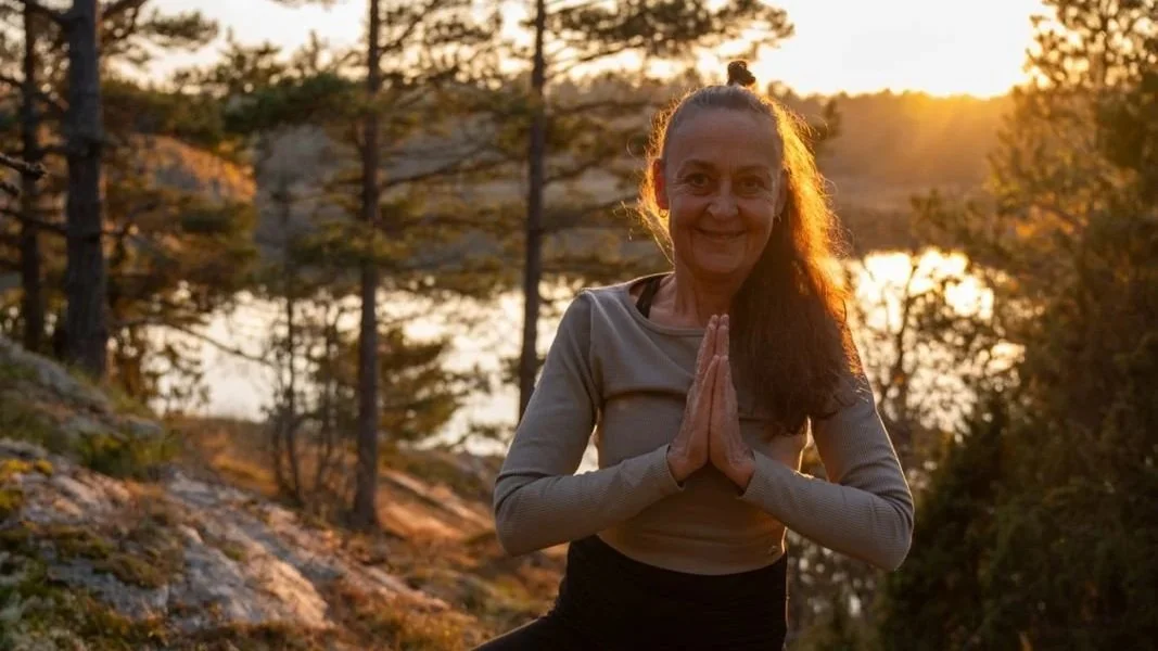 Cecilia Douglas utför yoga eller meditation utomhus vid solnedgången i naturen med träd och vattendrag.