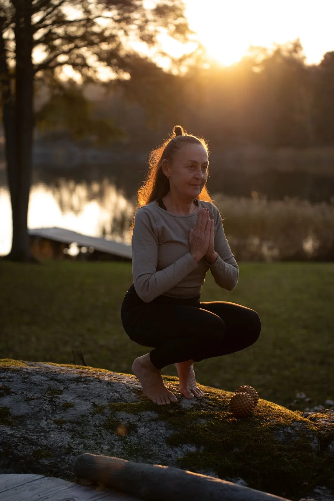 Cecilia Douglas i lugn yogaställning utomhus vid solnedgången, på ett berg vid vatten.