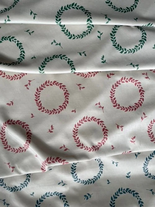 Fabric with a pattern of red and green laurel wreaths and small birds.