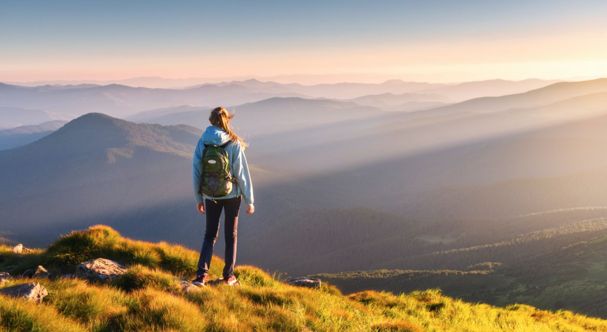 A woman with a backpack standing on the edge of a cliff overlooking beautiful mountains in the distance