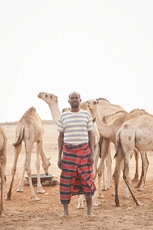 photograph of a man standing in front of camels in ethiopia