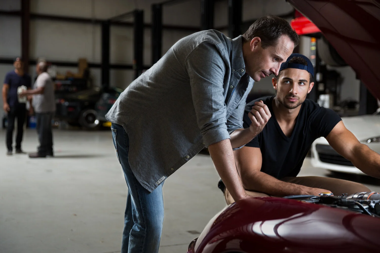 Photograph of men looking under car hood