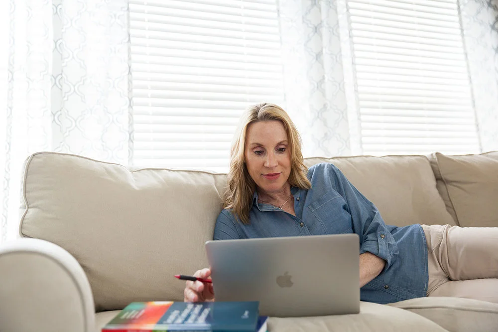 photograph of woman lying on couch looking at computer