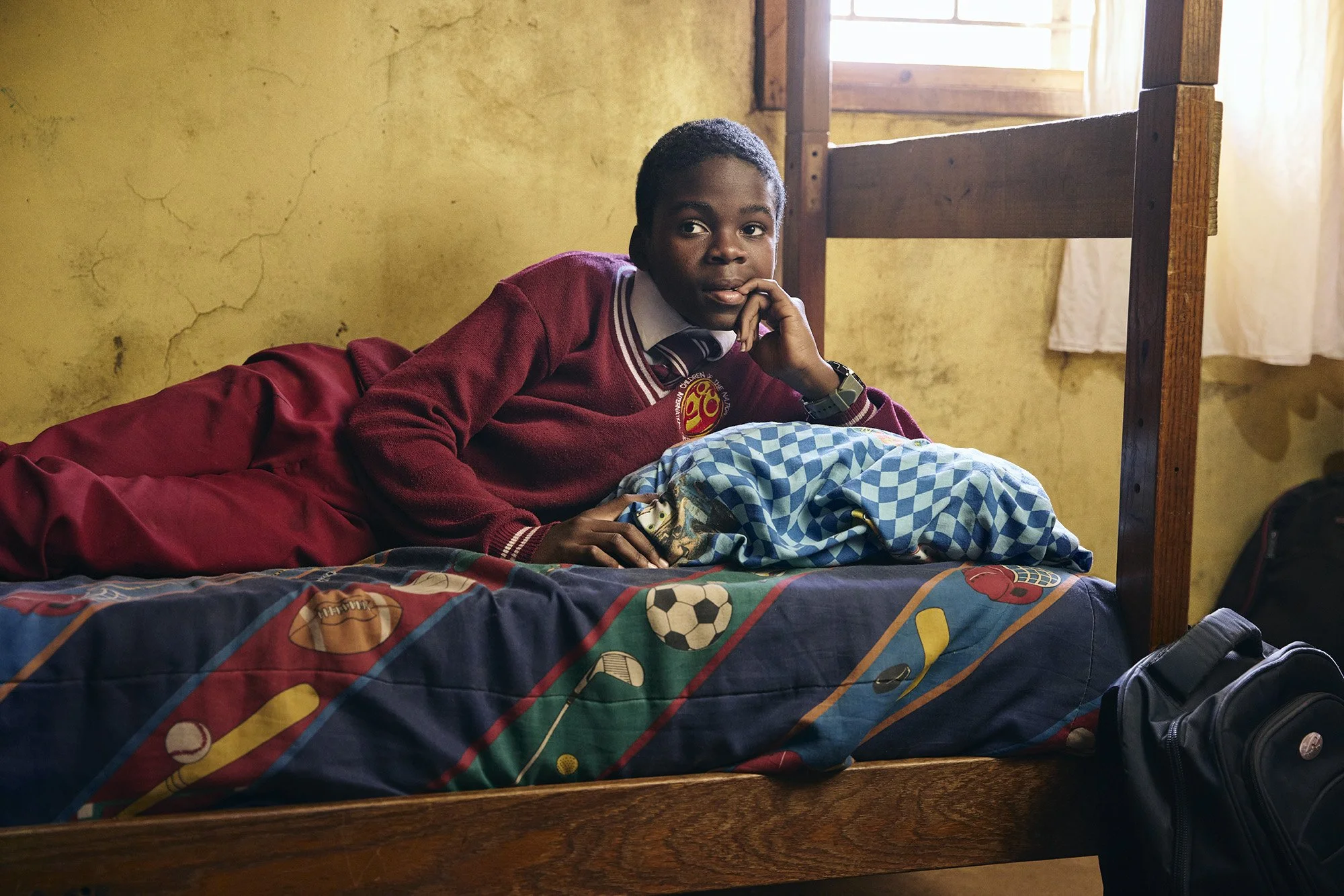 photo of african boy at boys school lying in bed chewing his nails nervously