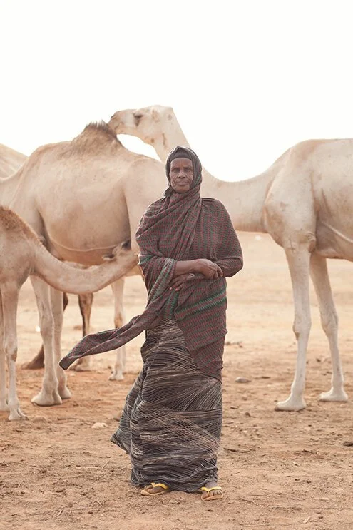 photograph of somali woman standing with camels