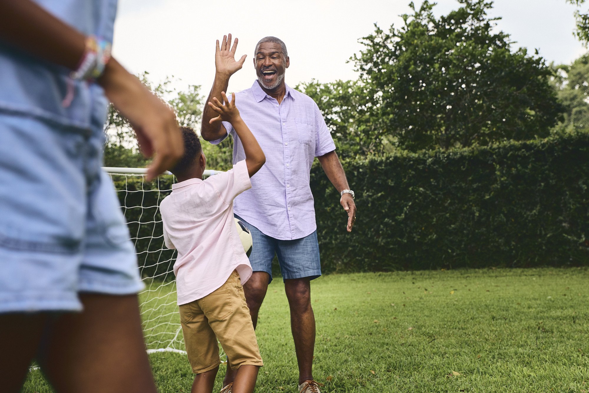 Grandfather high-fives his grandson at a backyard soccer net, healthcare lifestyle photography in Central Florida