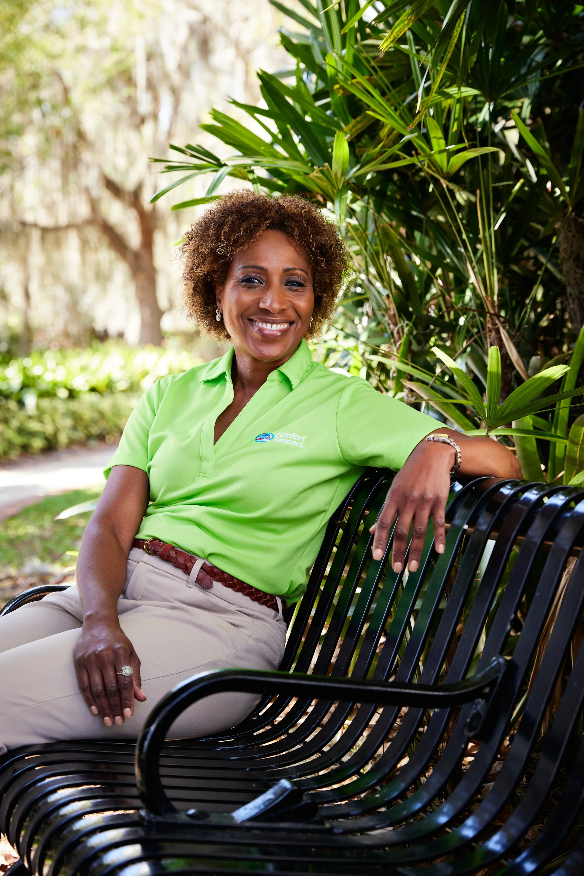 Smiling person sitting on a park bench wearing a green shirt in a garden setting.