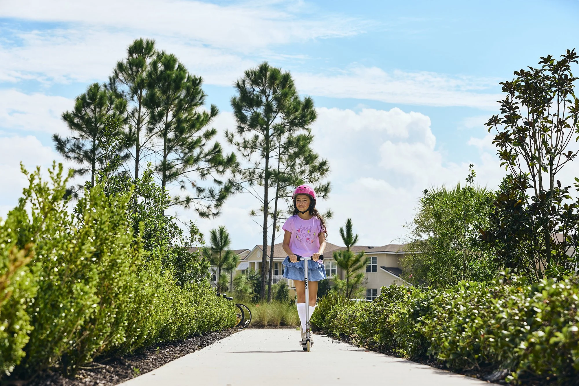 Lifestyle photo of a girl on scooter on landscaped path in a master-planned community