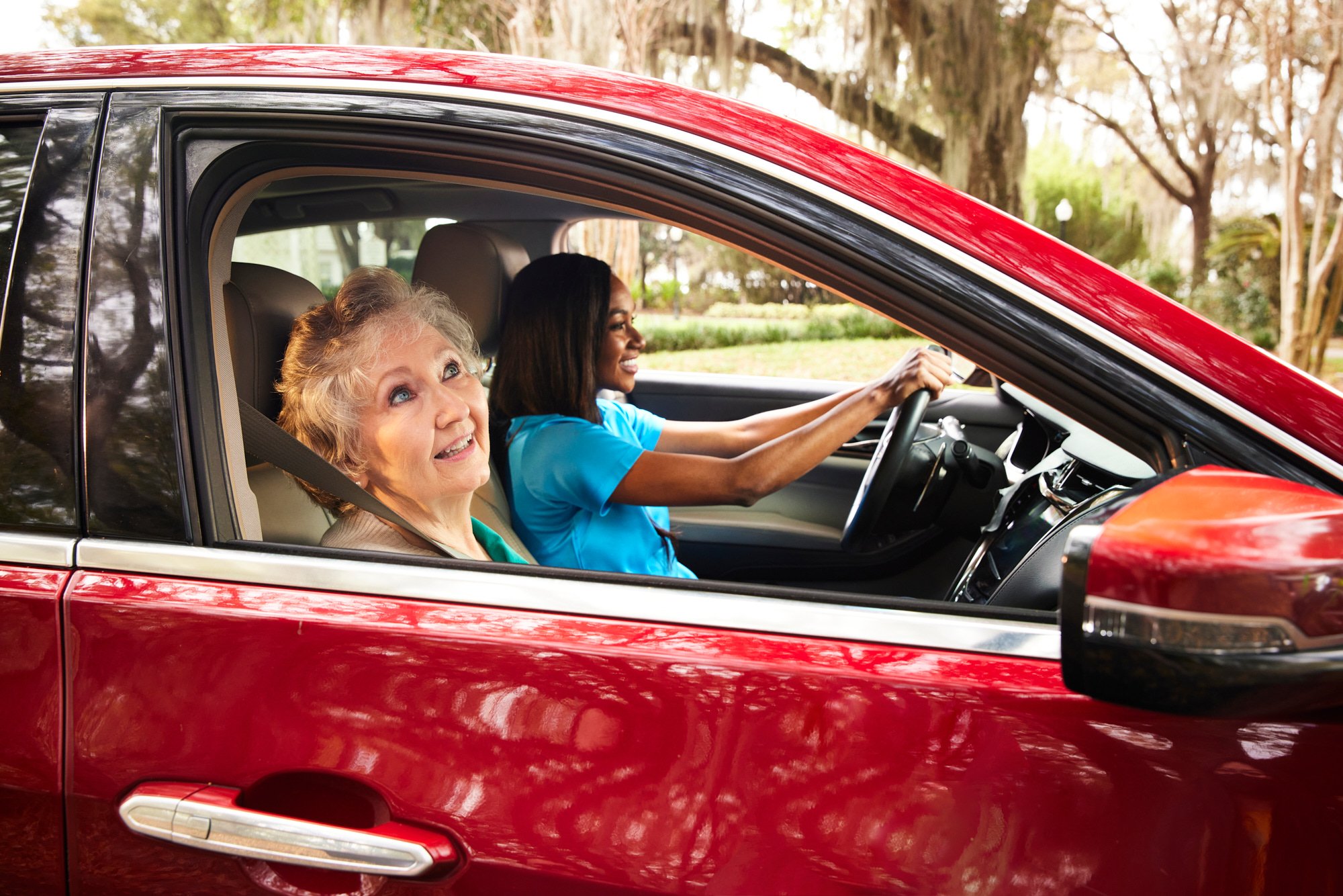 Two women in a red car, with a senior woman in the passenger seat and a younger woman driving.