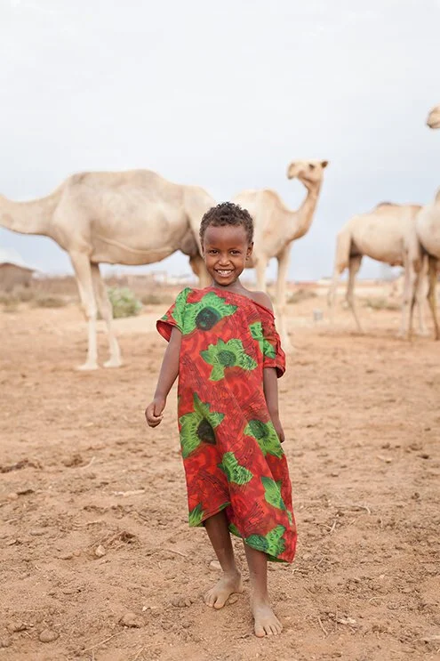 photograph of young girl in front of camels in desert in ethiopia