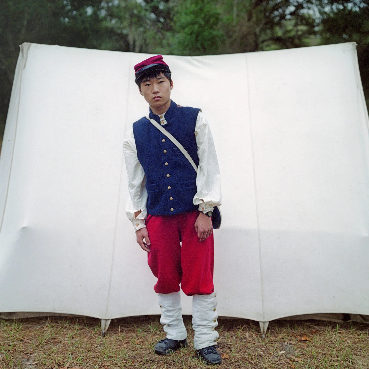 Person in historical military uniform standing in front of a canvas tent outdoors.