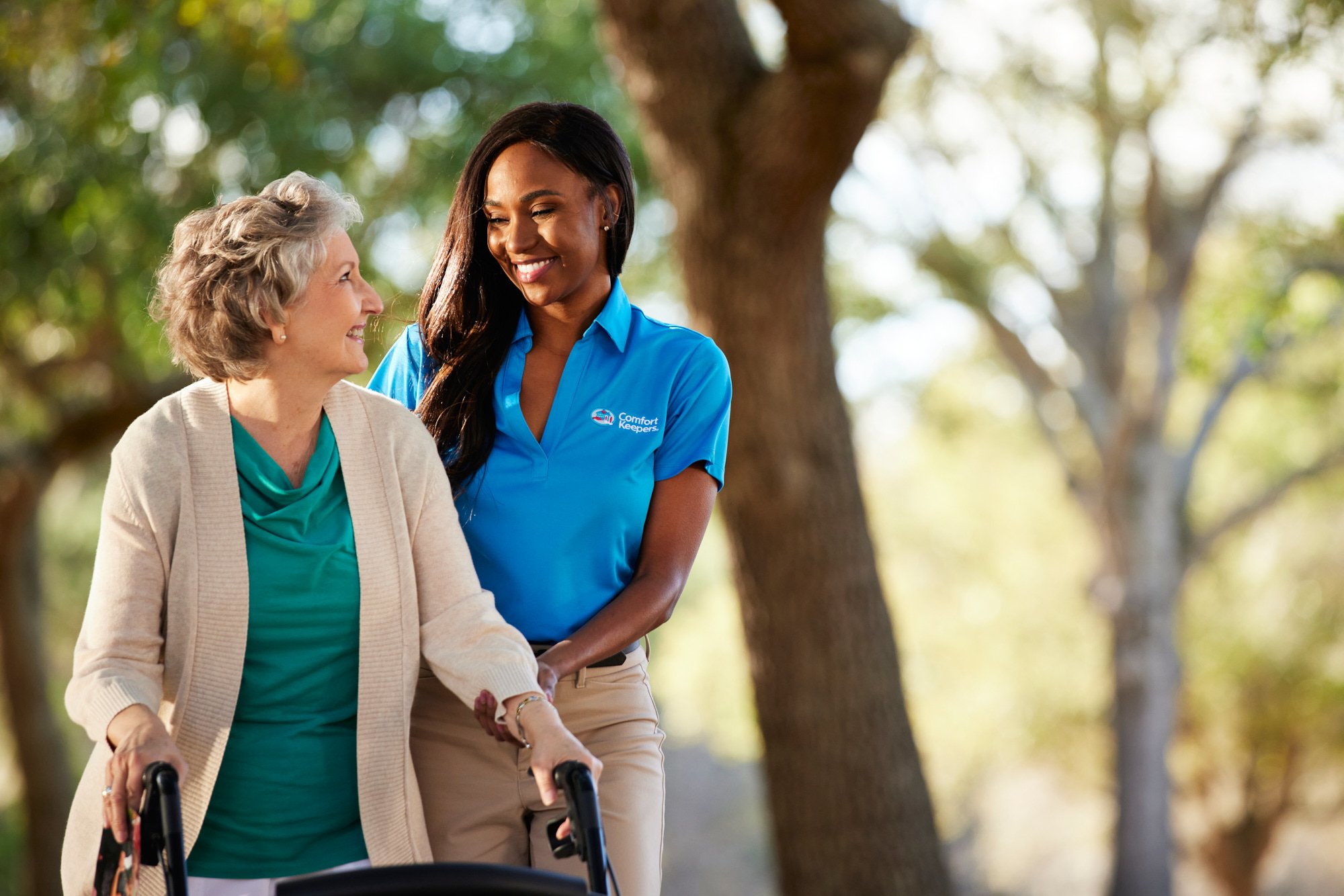 Elderly woman with a walker assisted by a caregiver in a blue shirt outdoors