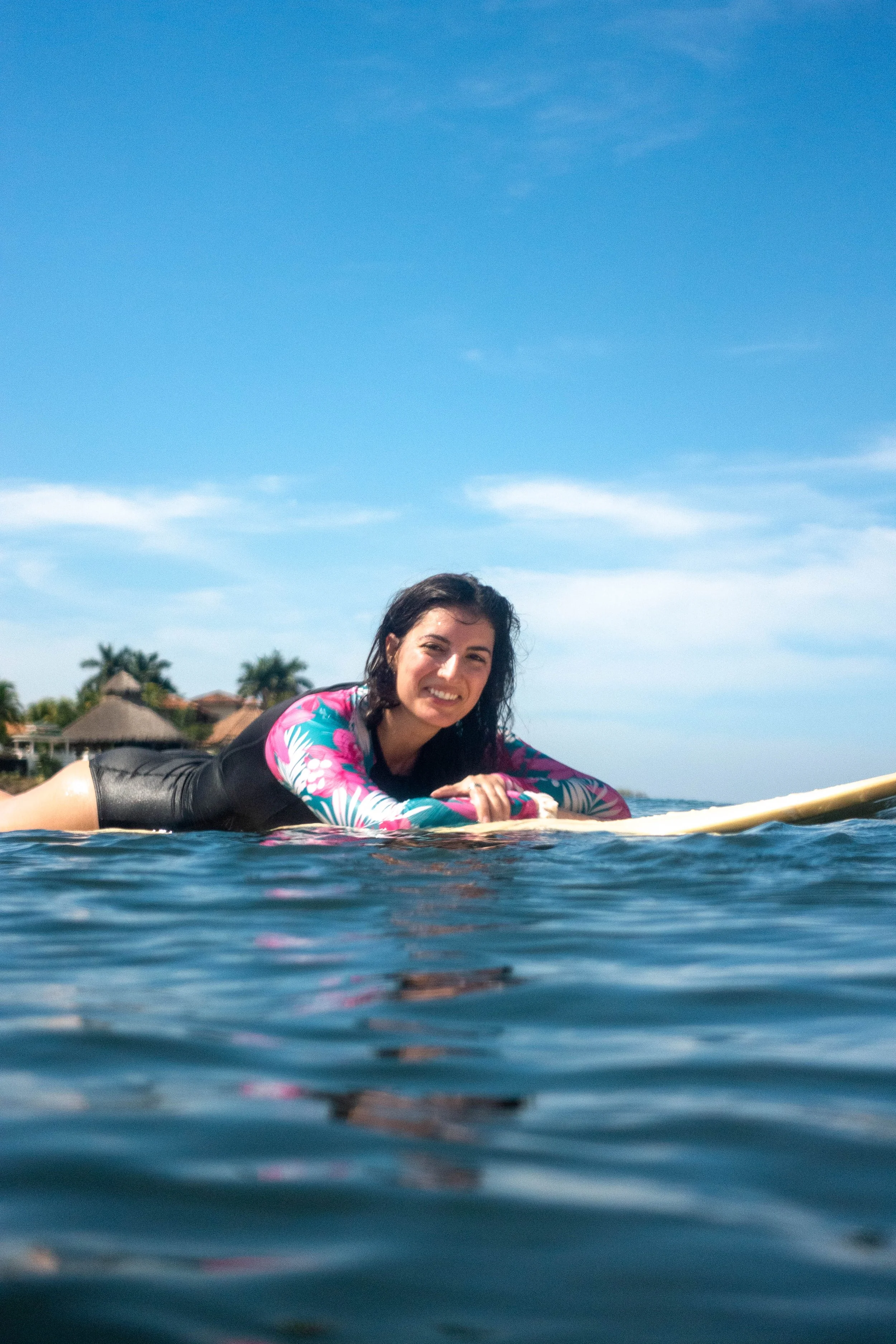 Smiling surfer paddling a longboard with the retreat cabañas behind during a surf lesson in Nicaragua