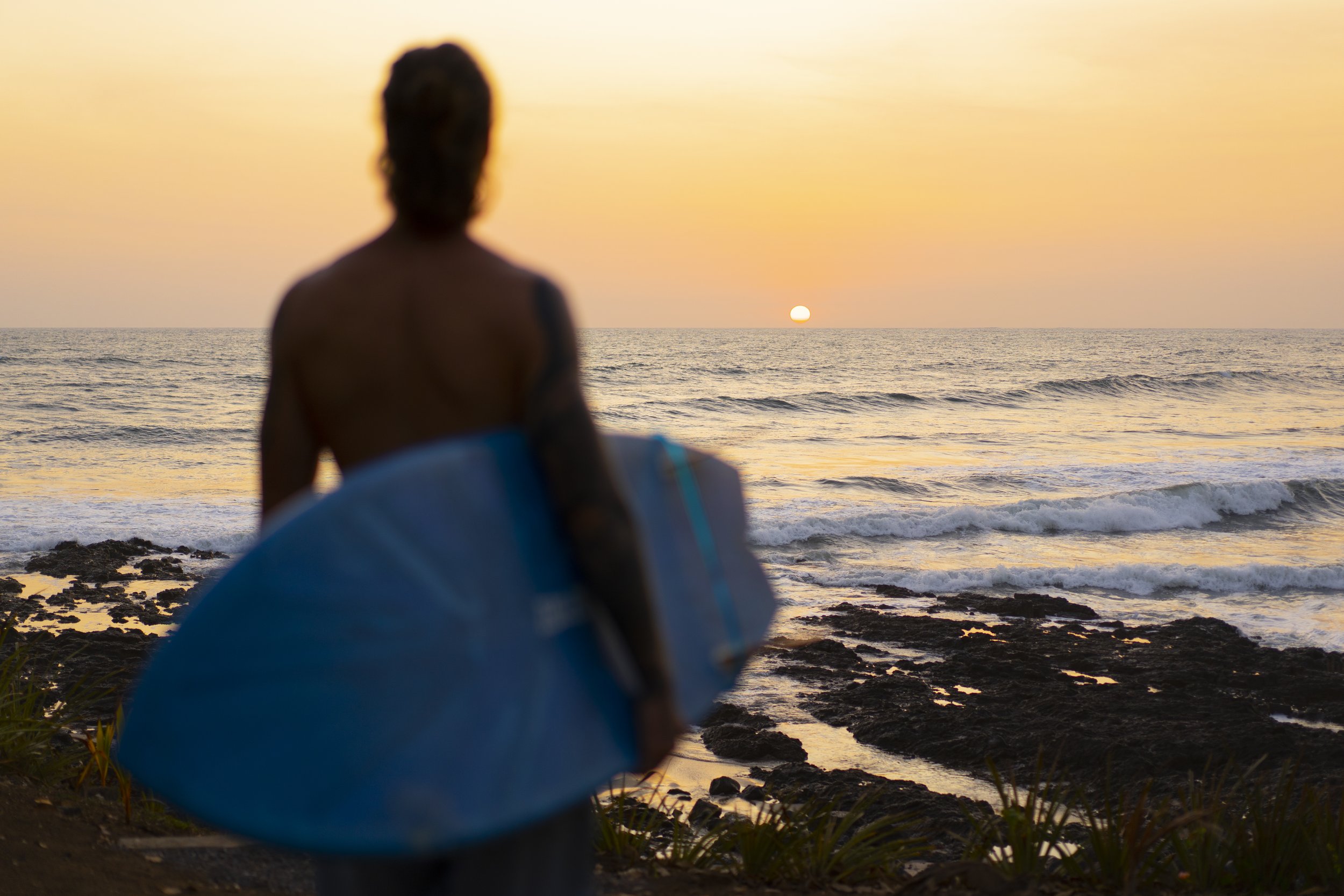 Surfer with board under his arm watching the uncrowded waves at sunset on Nicaragua's Pacific coast surf camp
