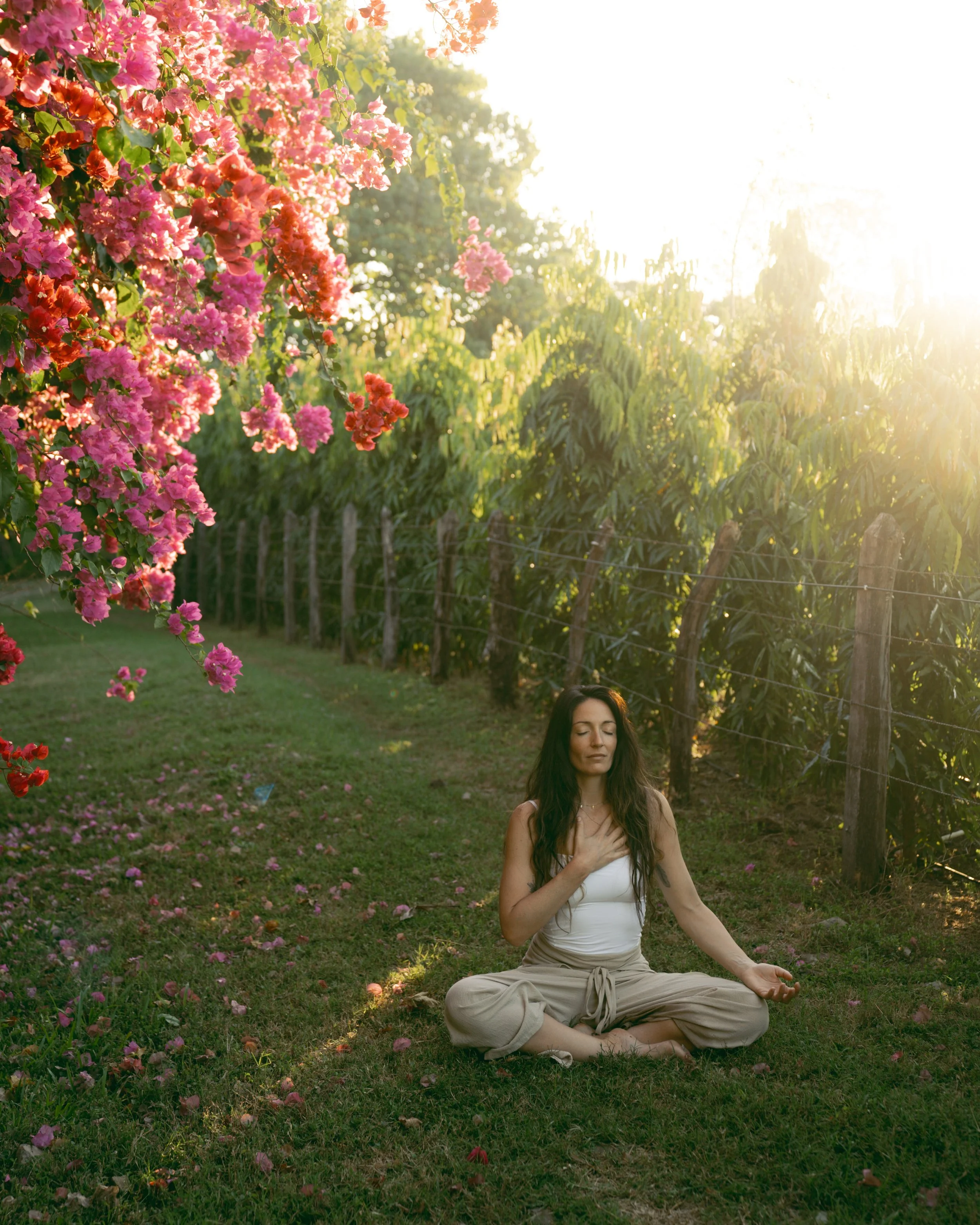 Woman meditating cross-legged in a flowering garden at sunset during a yoga retreat in Nicaragua
