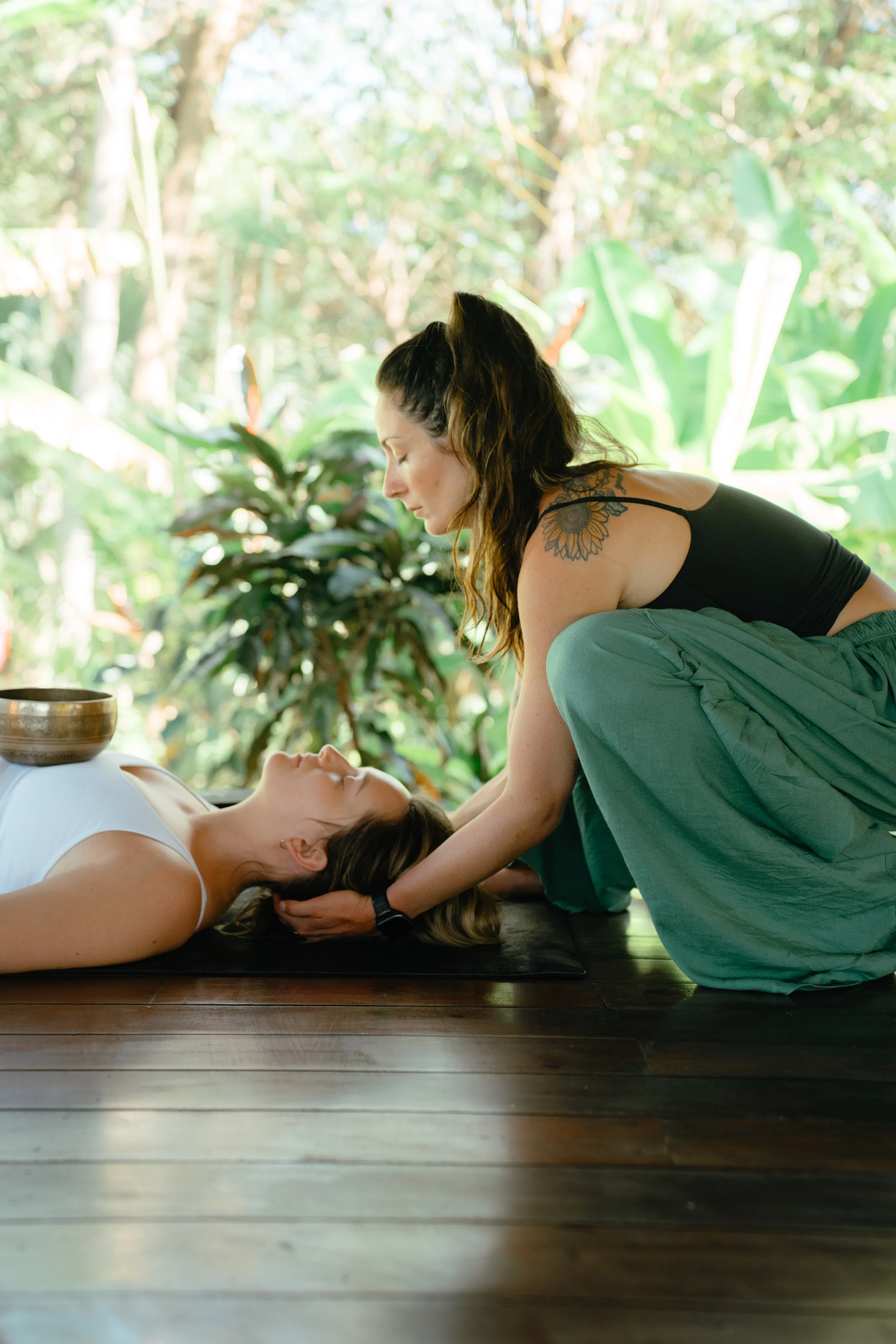 Practitioner cradling a guest's head with a singing bowl resting on her chest during a healing session at a retreat in Nicaragua