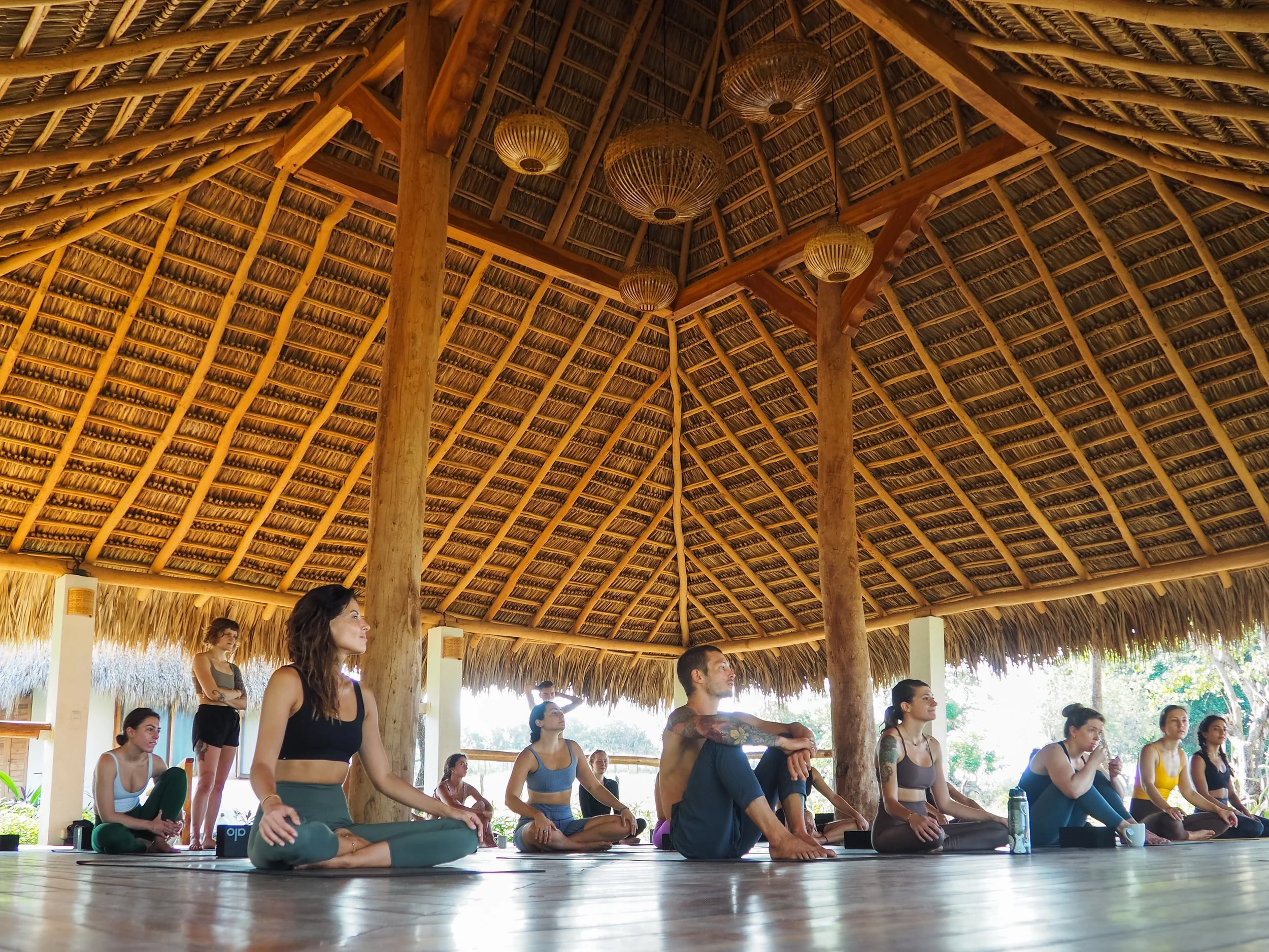 Full yoga retreat group seated for practice in the open-air shala under a thatched roof at Still Salty Escape in Nicaragua