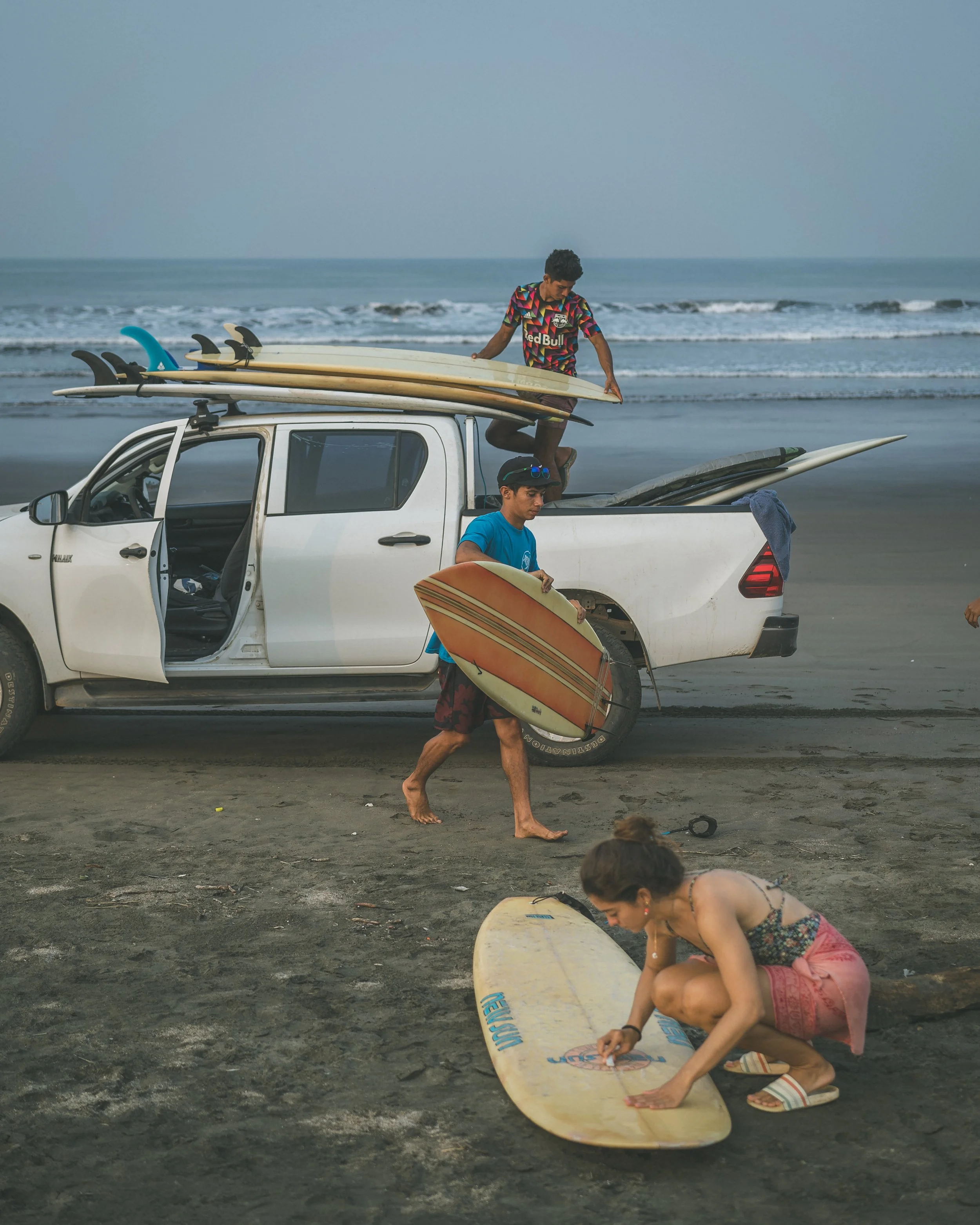 Surfer passing a longboard up onto a truck on the beach at a surf retreat in Nicaragua