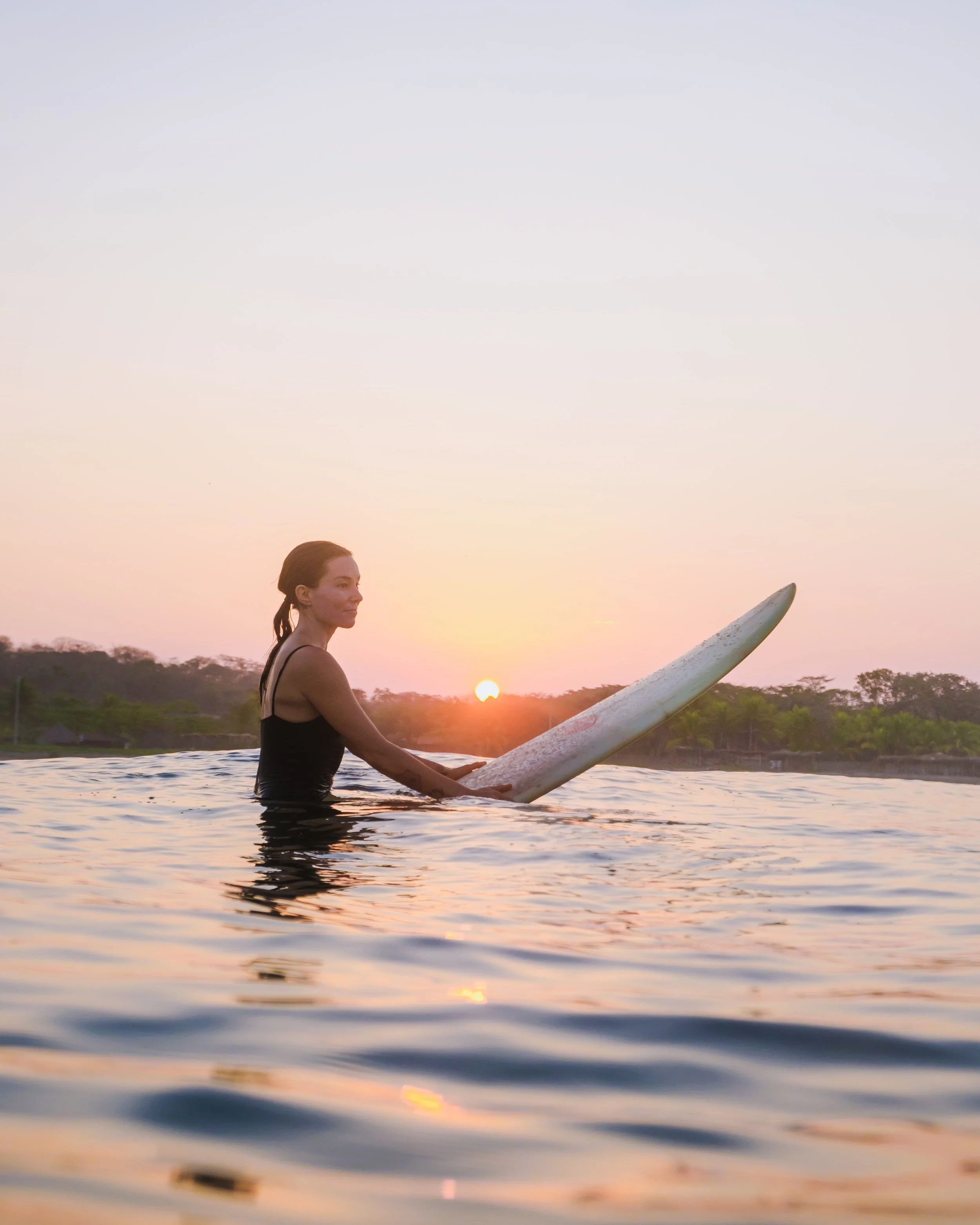 Woman on her surfboard at sunrise in the uncrowded waves of Nicaragua's Pacific coast surf camp